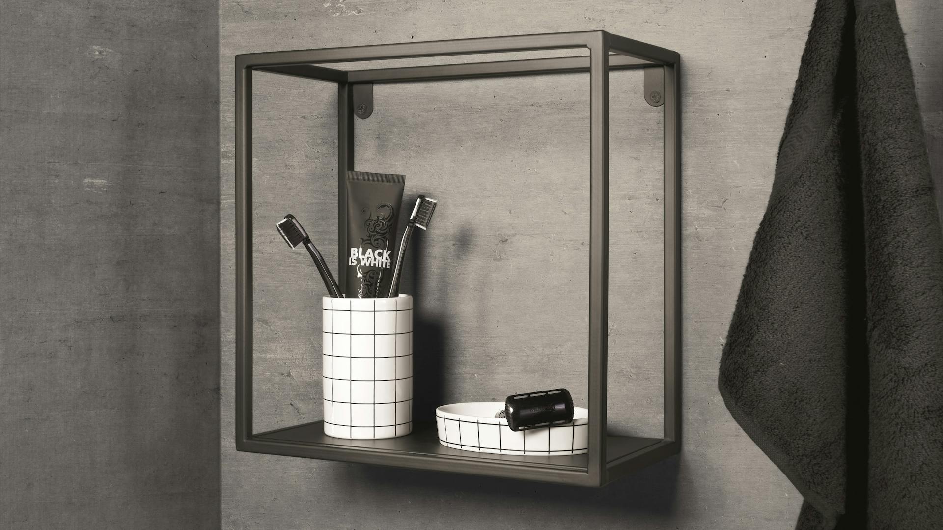 Beton-Bad mit Hängeregal und dunklen Dekoelementen sowie einem schwarzen Handtuch.