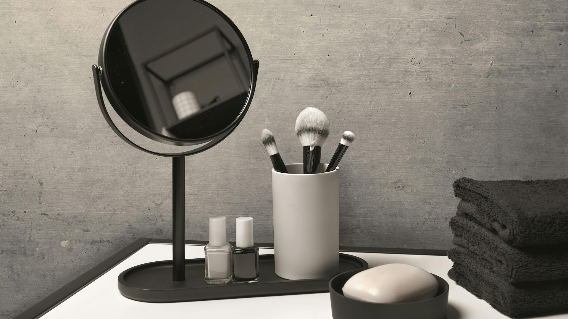 Beton-Bad mit schwarzen Dekoelementen, Spiegel und Seifenschale neben Handtüchern.