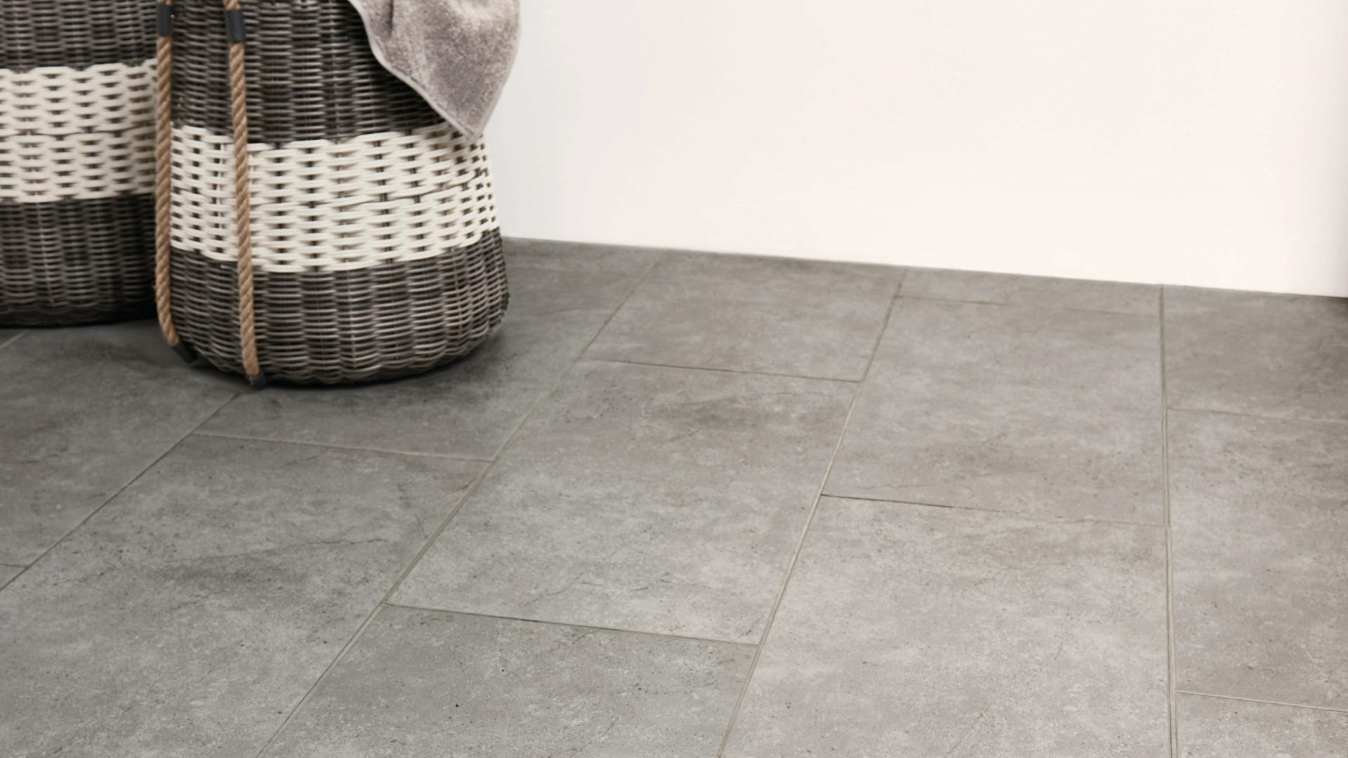 Graue Bodenfliesen vor einer ungefliesten Wand.
