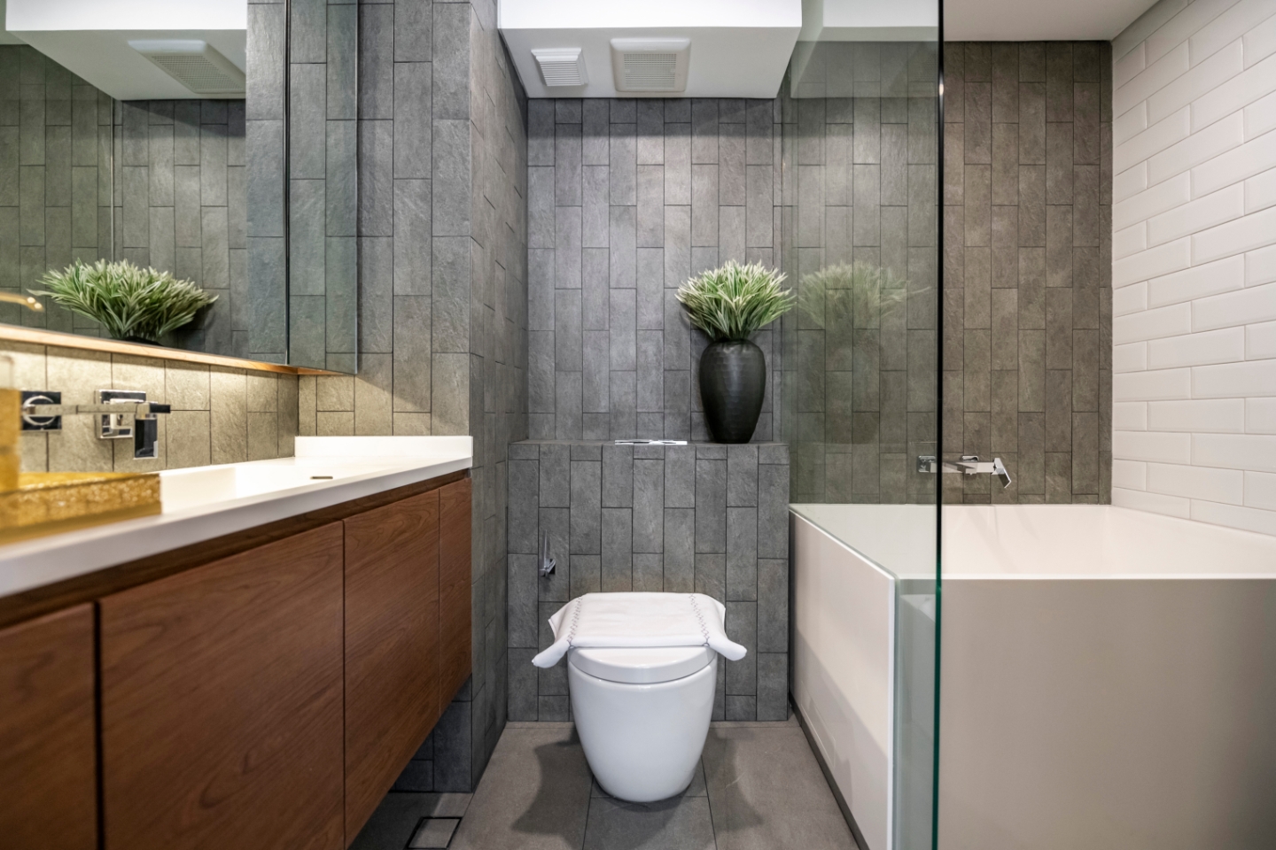 Bagno moderno con sanitario, vasca con parete in vetro e lavabo con rivestimento in legno.