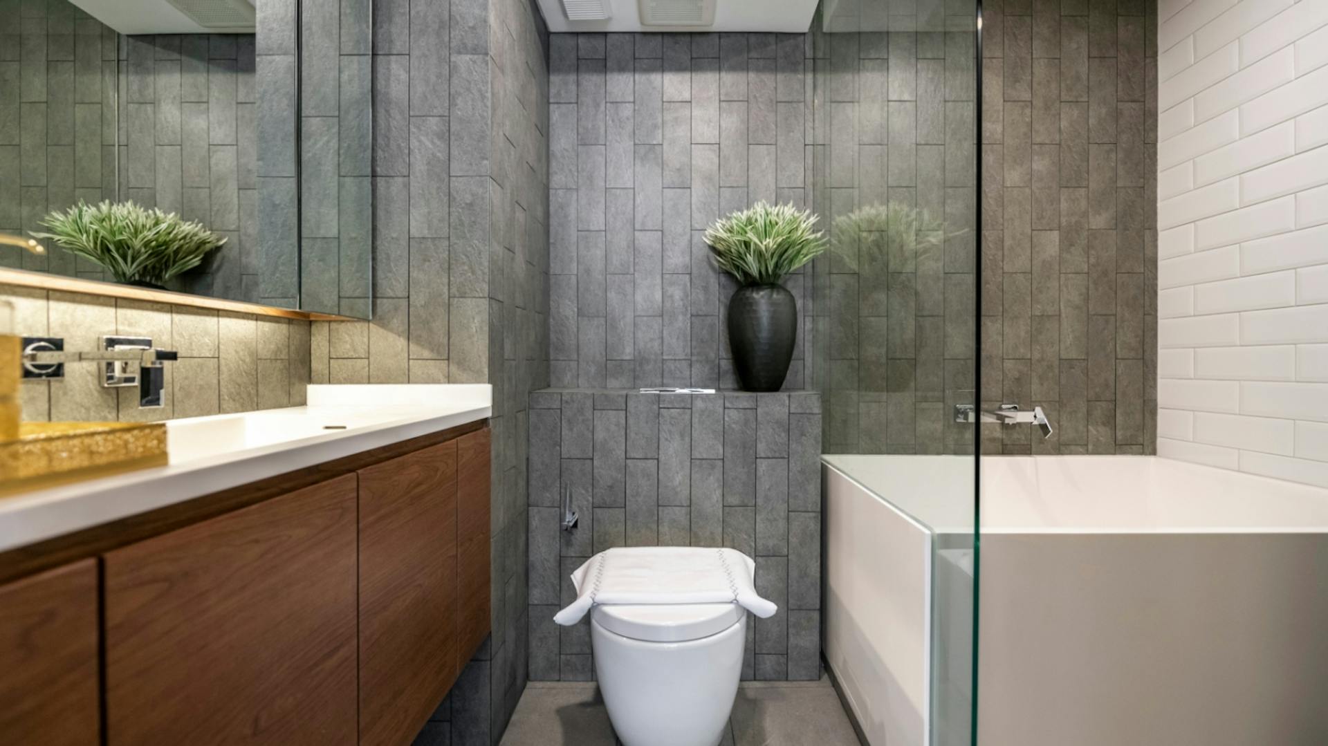 Moderní koupelna s toaletou, vanou se skleněnou zástěnou a skříňkou pod umyvadlem s dřevěným obložením.