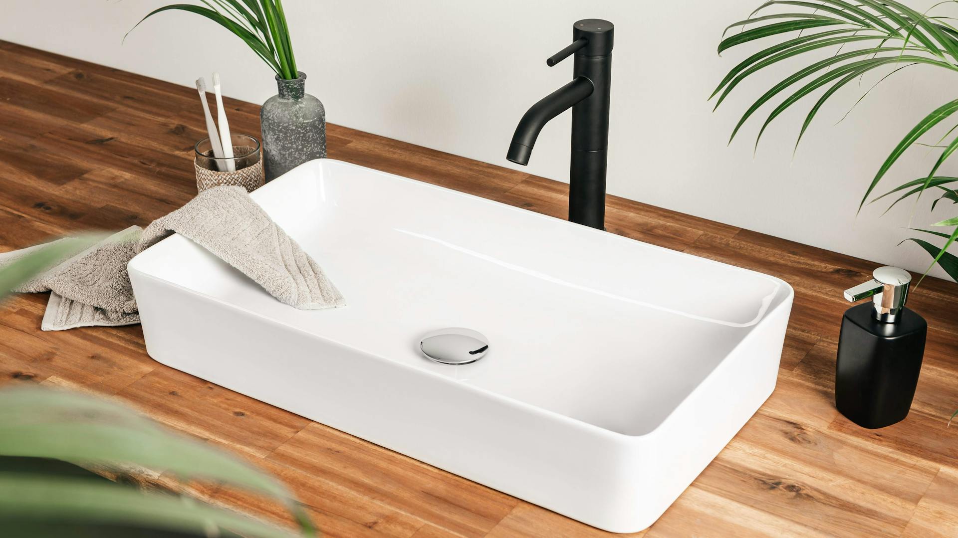 Natürliches bad mit Waschbecken mit dunkler Armatur auf Holzfläche.