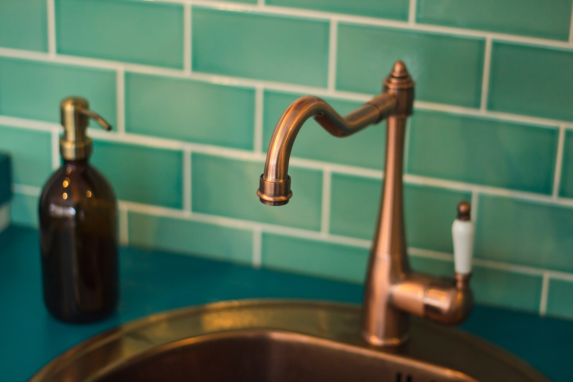 Bronzefarbener Wasserhahn vor einer grün gekachelten Wand.