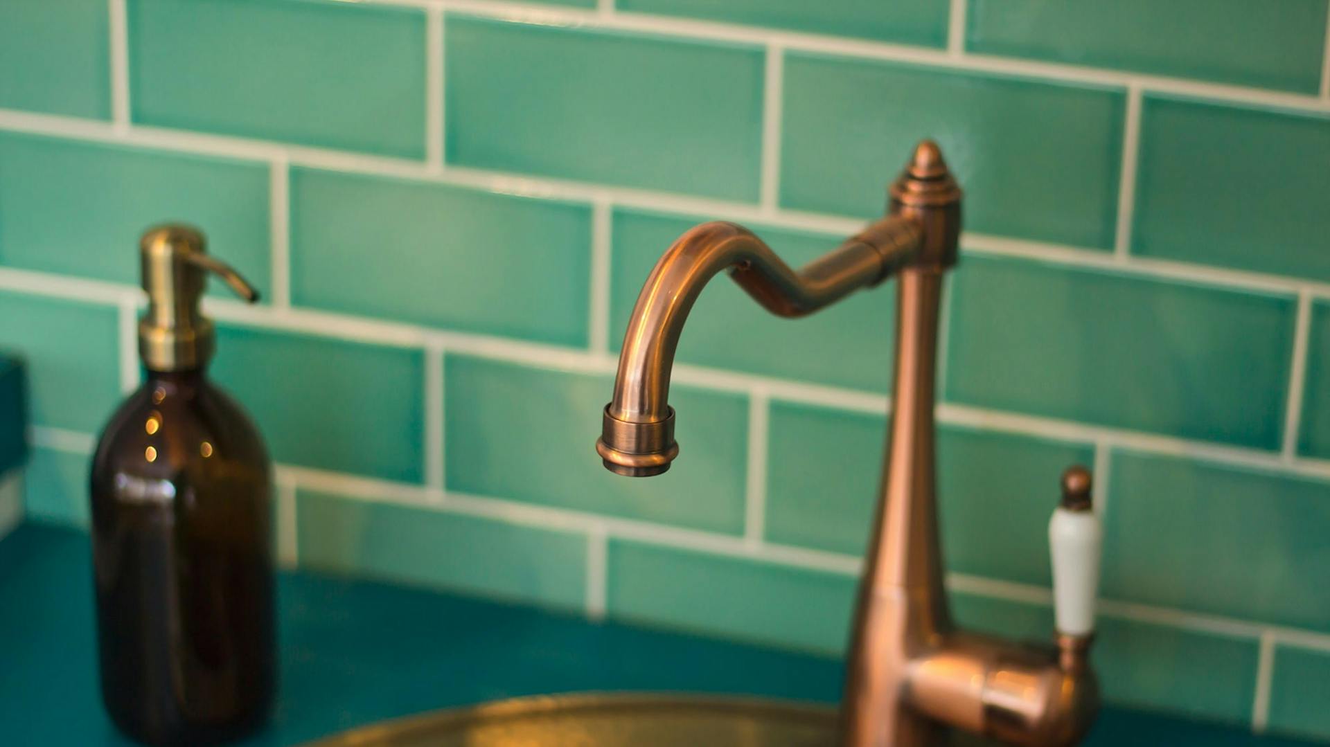 Bronzefarbener Wasserhahn vor einer grün gekachelten Wand.