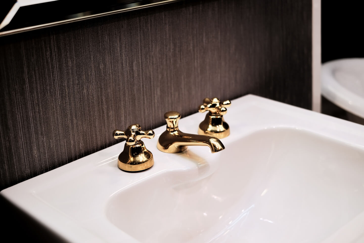 Weißes Waschbecken mit goldenem Wasserhahn in schwarzem Bad.