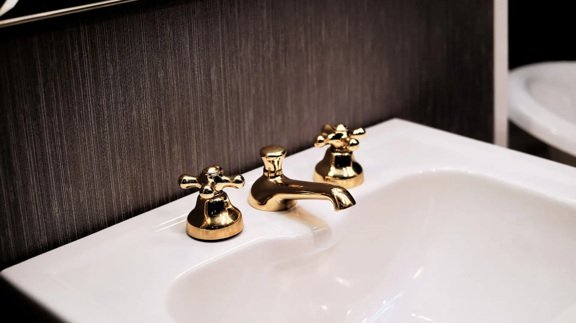 Weißes Waschbecken mit goldenem Wasserhahn in schwarzem Bad.