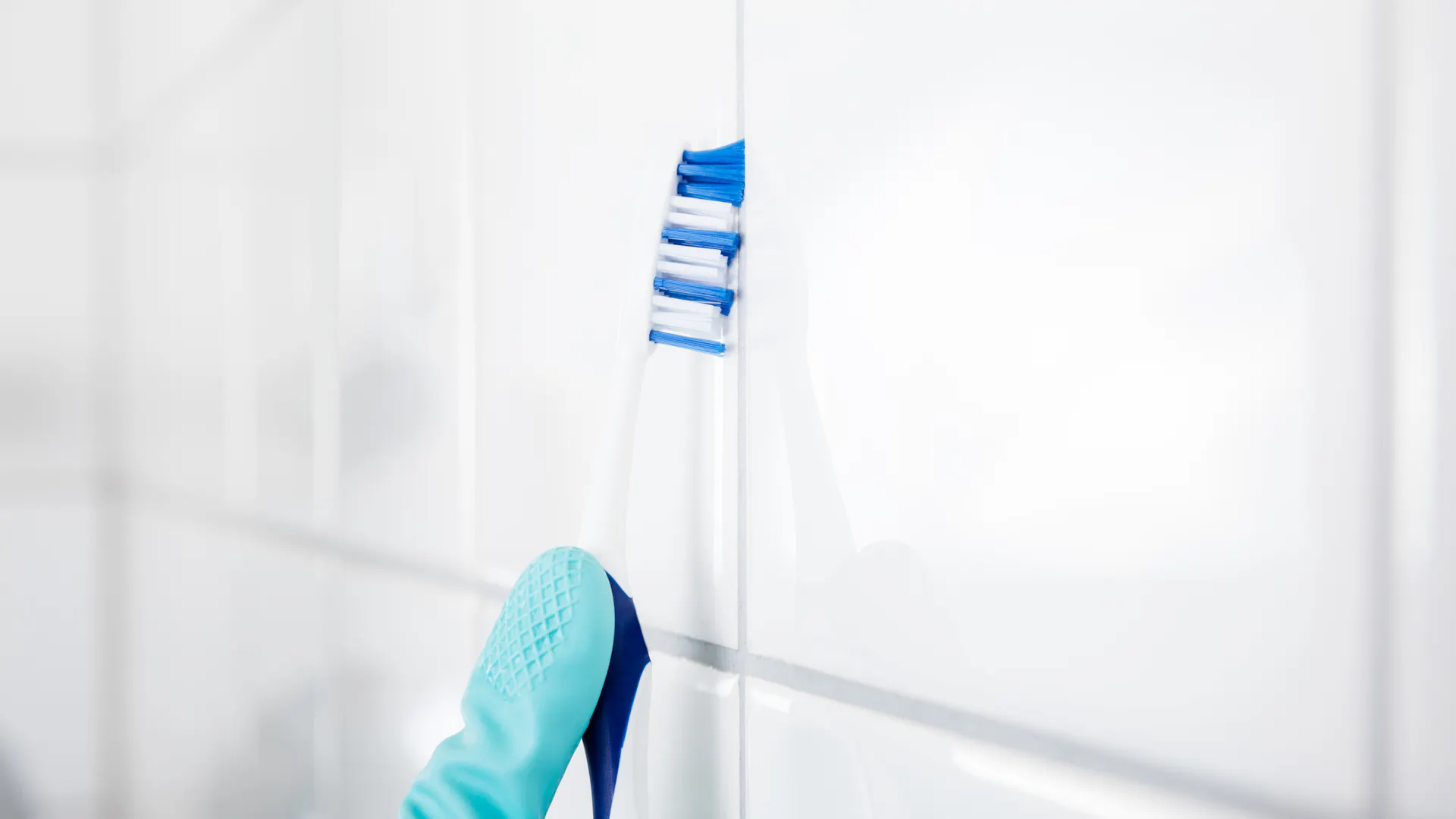 Una persona pulisce le fughe di un bagno con uno spazzolino da denti.