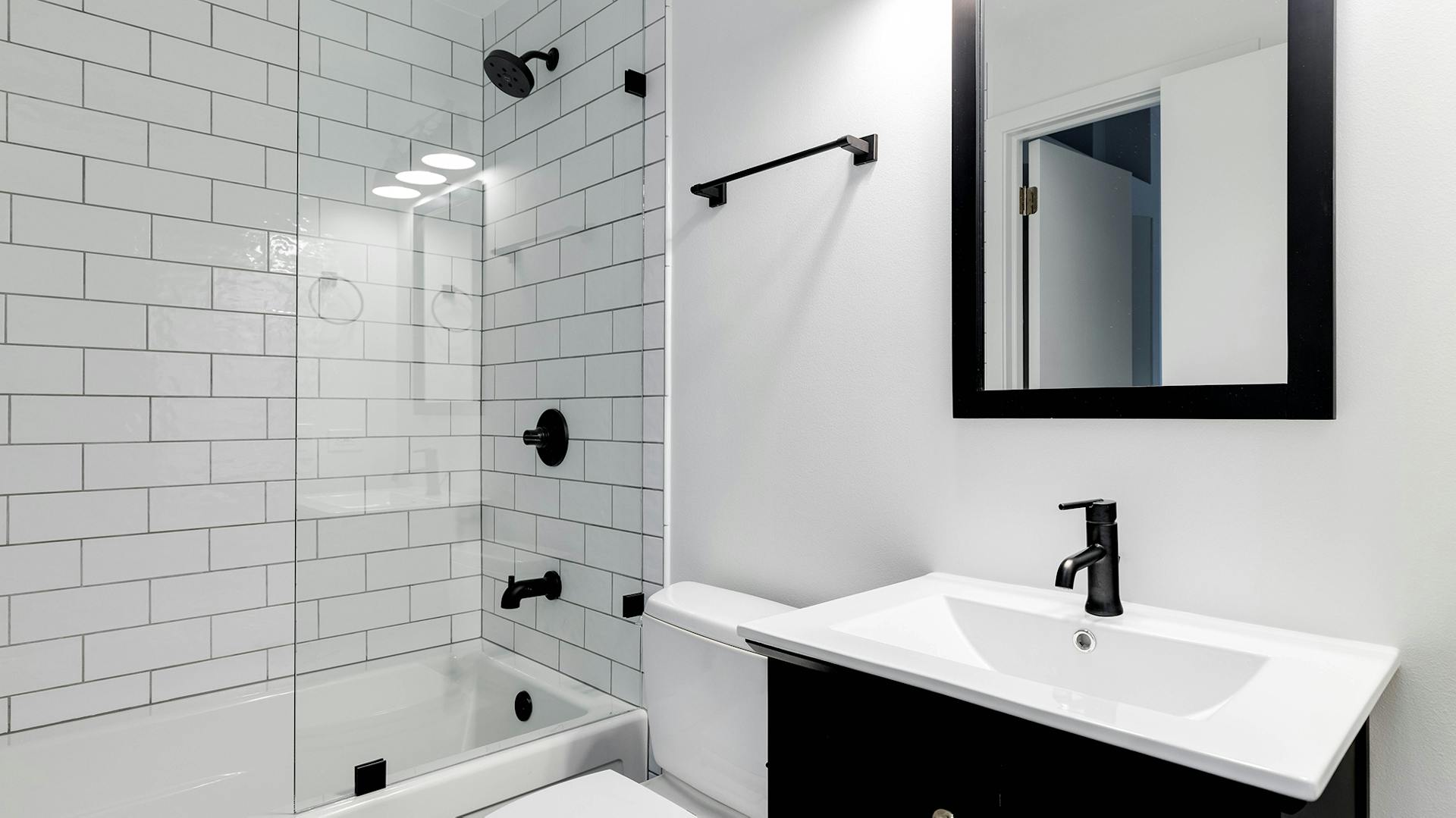 Weißes Bad mit Badewanne, dahinter weiße Fliesen. Schwarzer Waschtisch mit weißem Waschbecken.