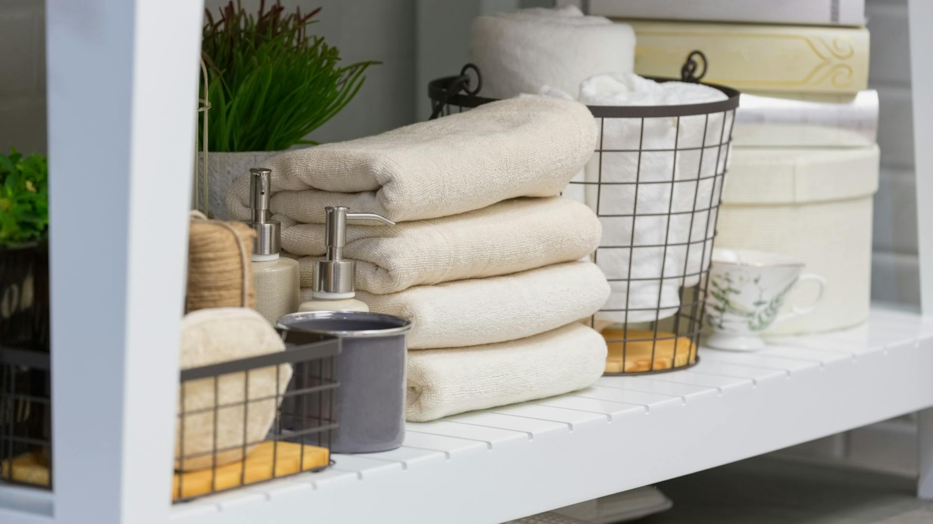 Weißes Regal mit Körben und hellen Handtüchern.