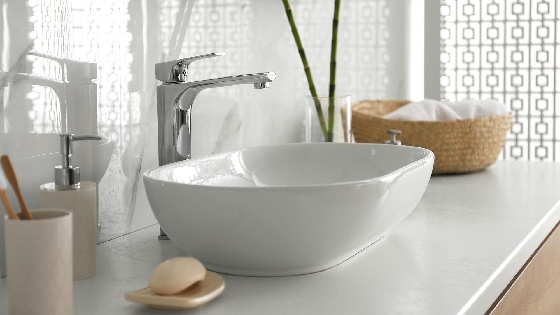 Weißes Waschbecken auf hellem Waschtisch. Daneben Zahnbürsten und Korb mit Handtüchern.