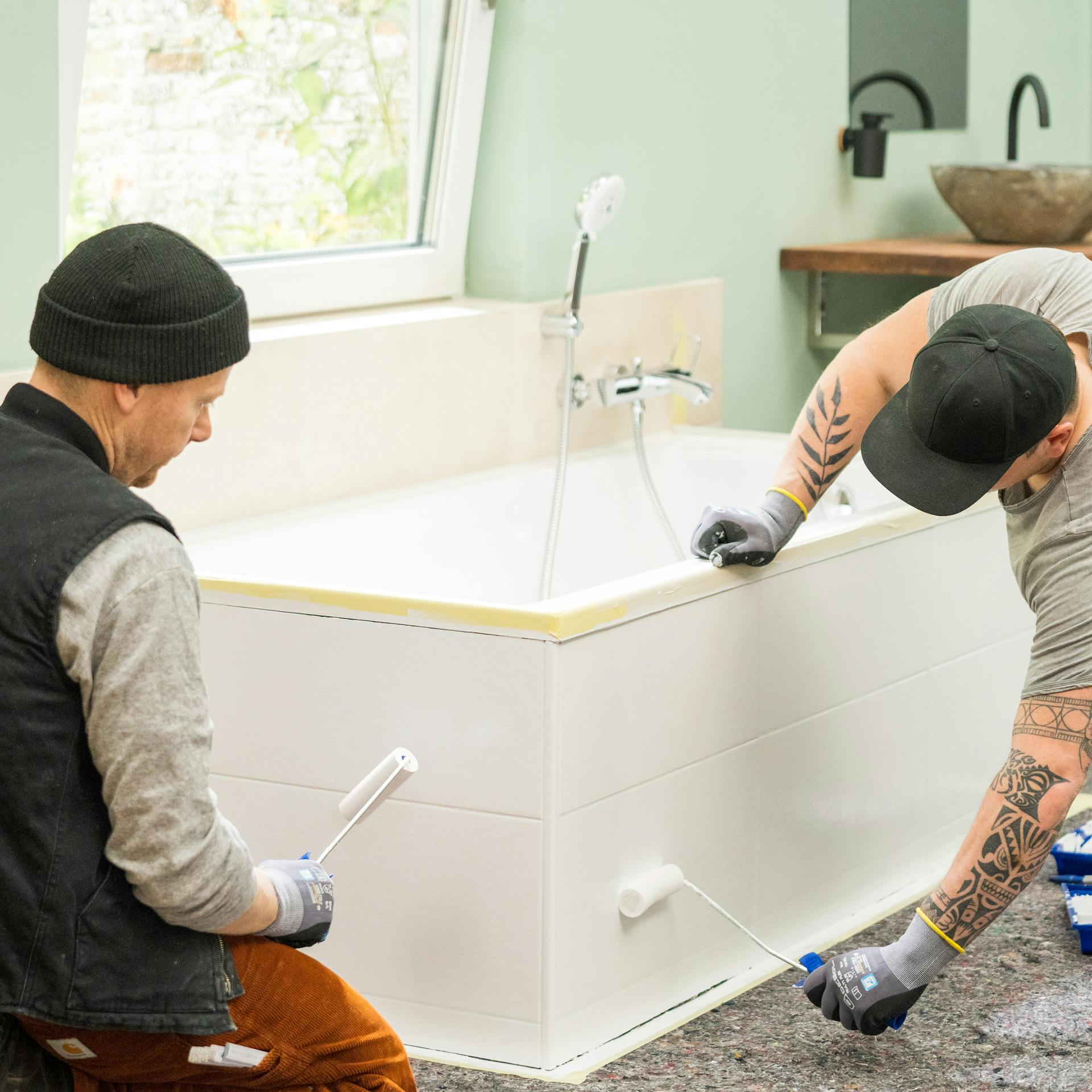 Heimwerker lackieren Badewannenfliesen mit einer Schaumstoffrolle.