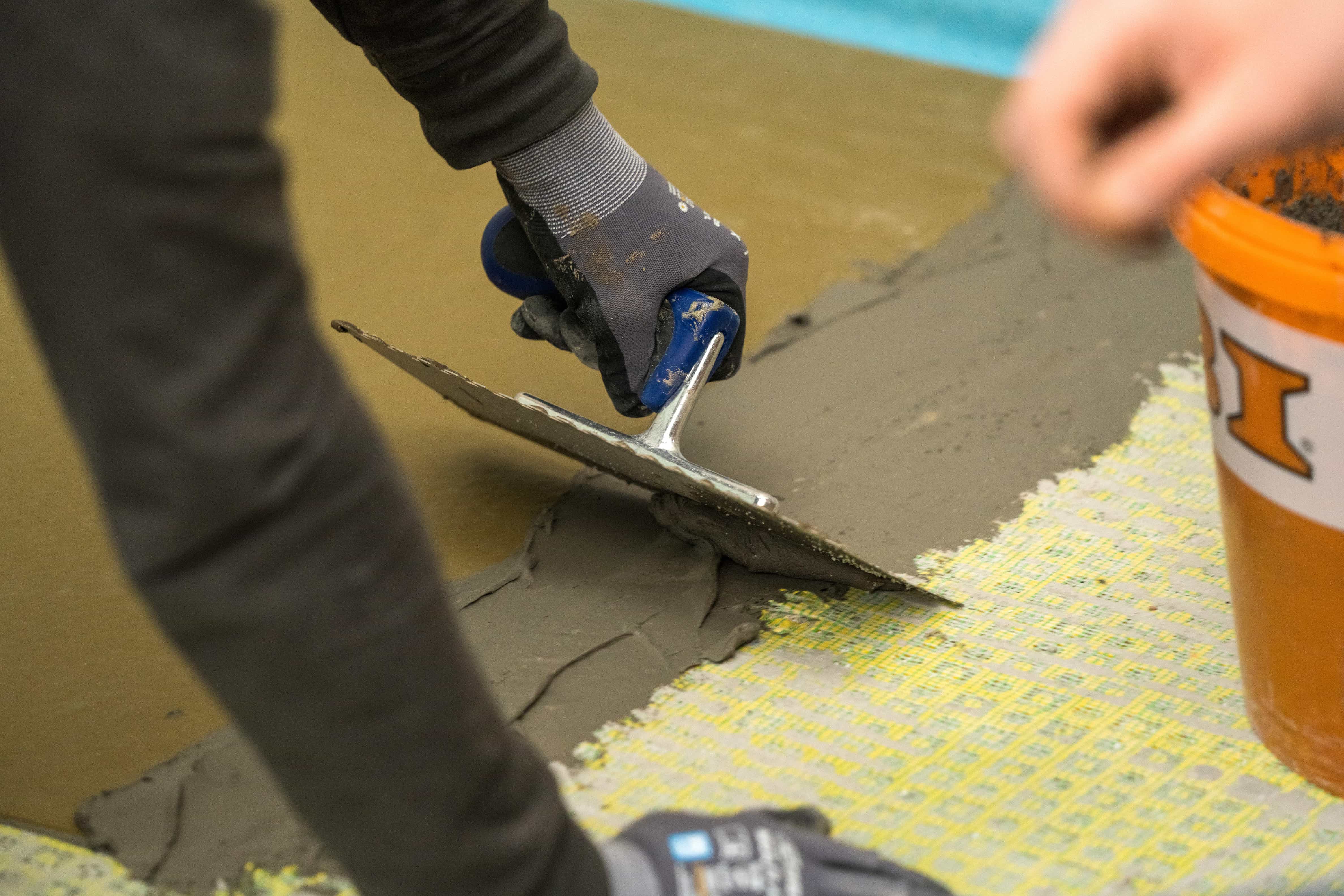 Valaki flexibilis csemperagasztóval kitölti a zuhanytálca éleinél lévő réseket.