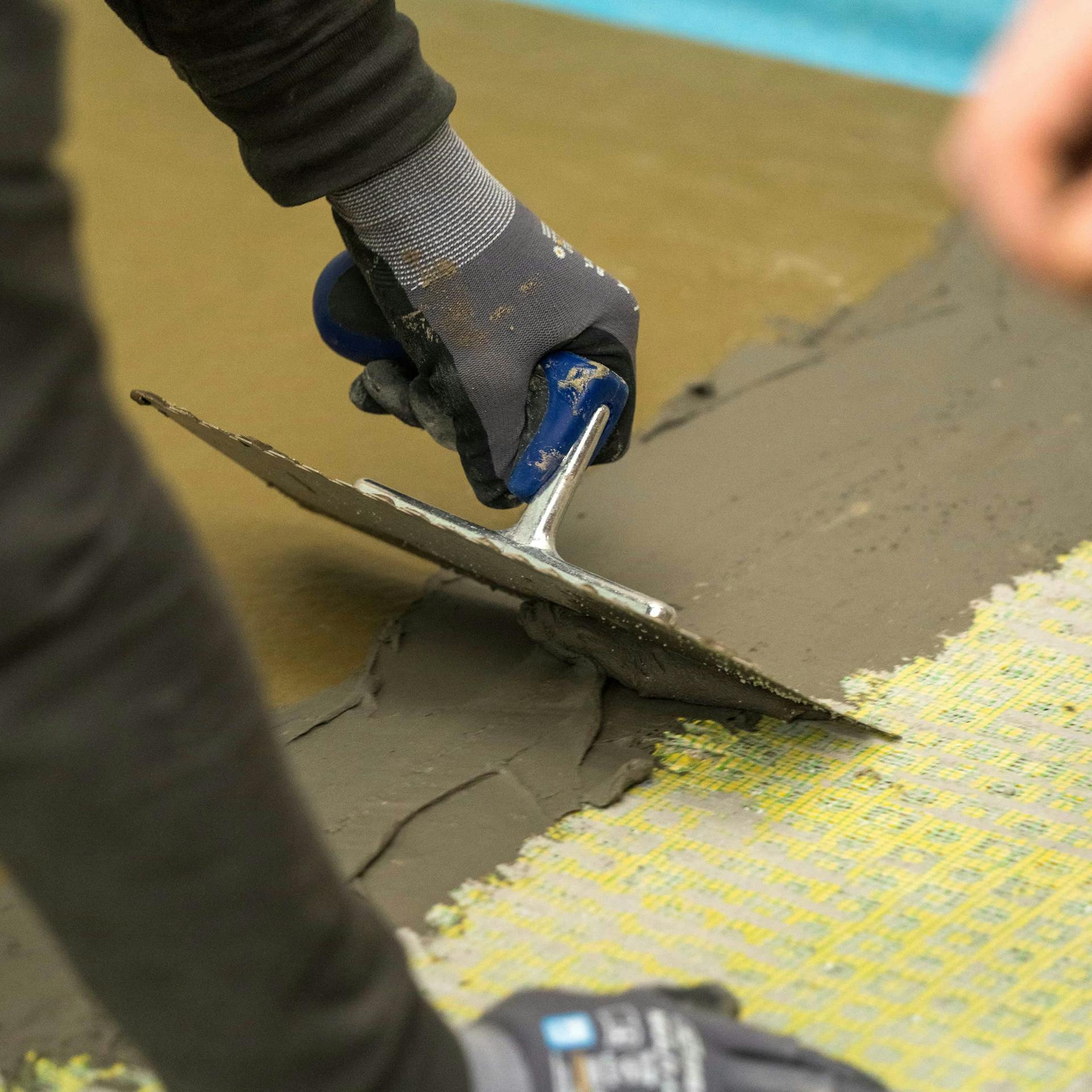 Valaki flexibilis csemperagasztóval kitölti a zuhanytálca éleinél lévő réseket.