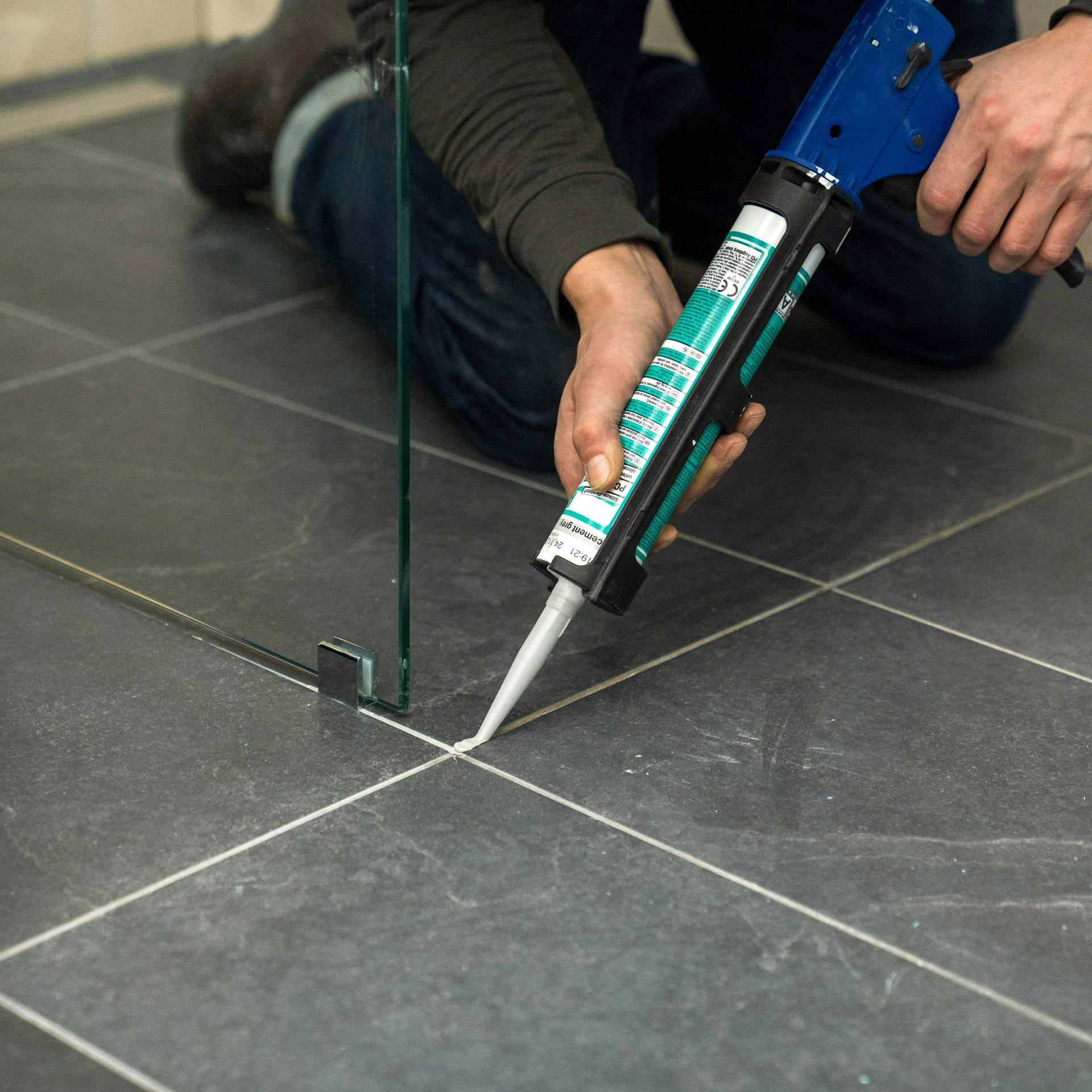 Valaki tömíti az épített zuhanyzó illesztéseit.