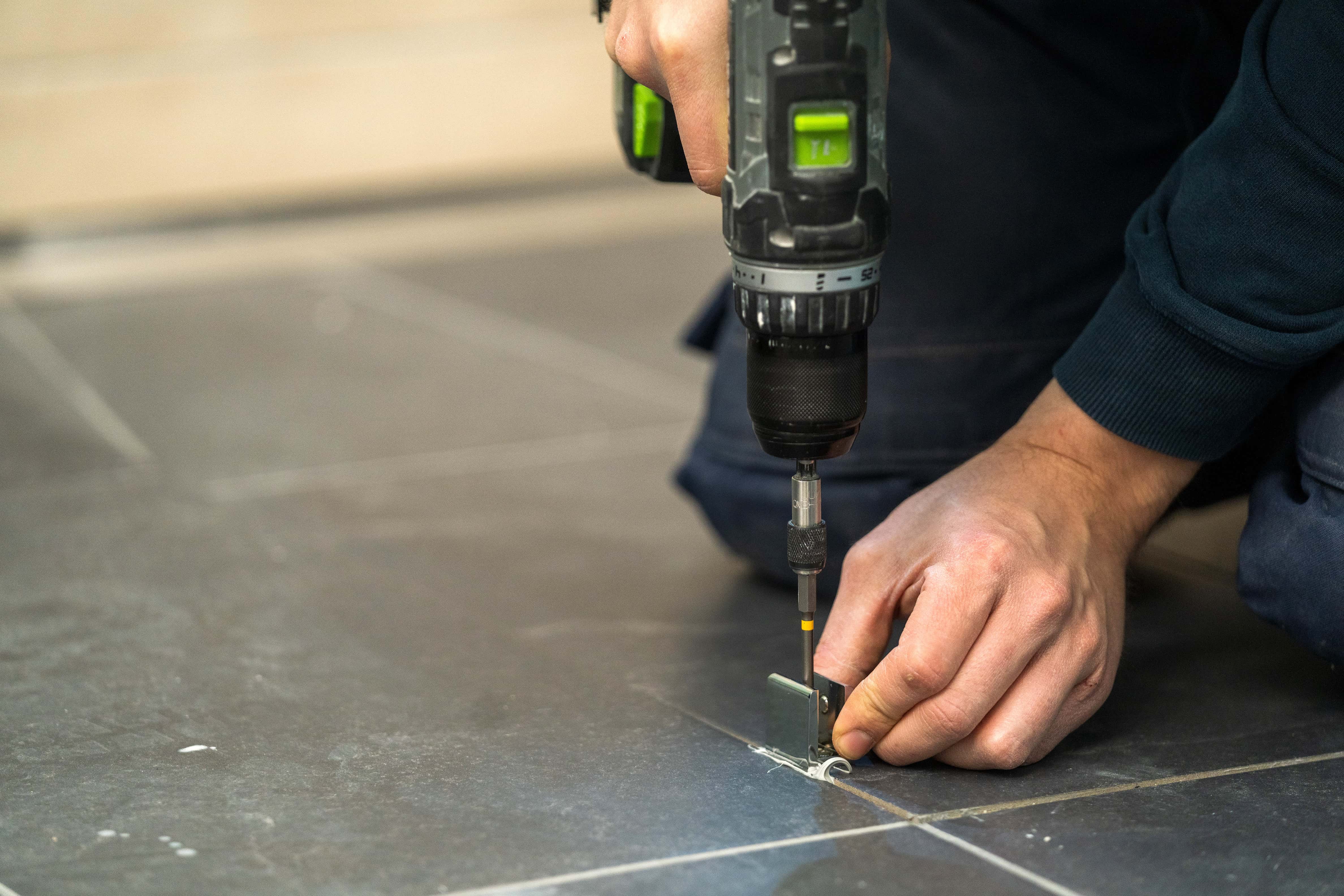 Valaki padlótartót szerel fel egy üveg zuhanyfalhoz.