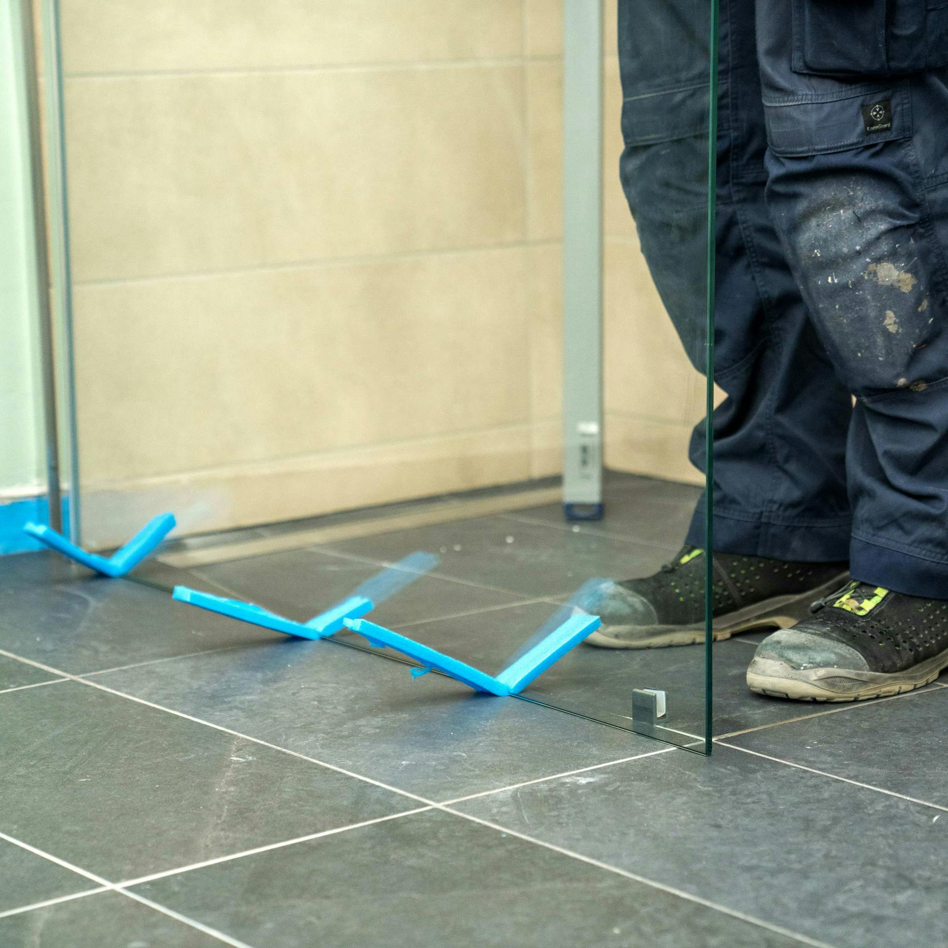 Valaki üveg zuhanyfalat állít be az épített zuhanyzóba.