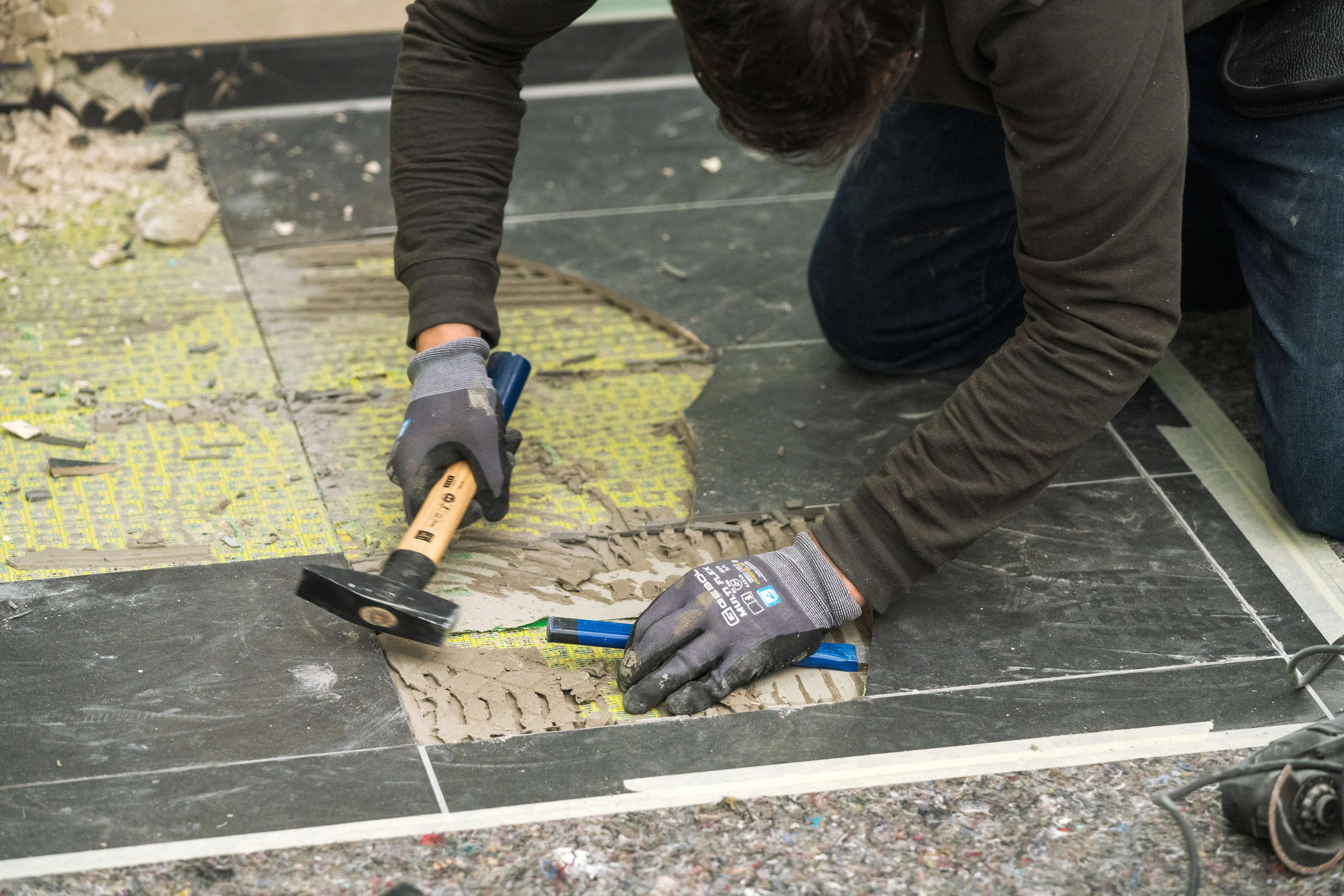 Valaki kalapáccsal és vésővel távolítja el a régi lapokat a zuhanyzóból.