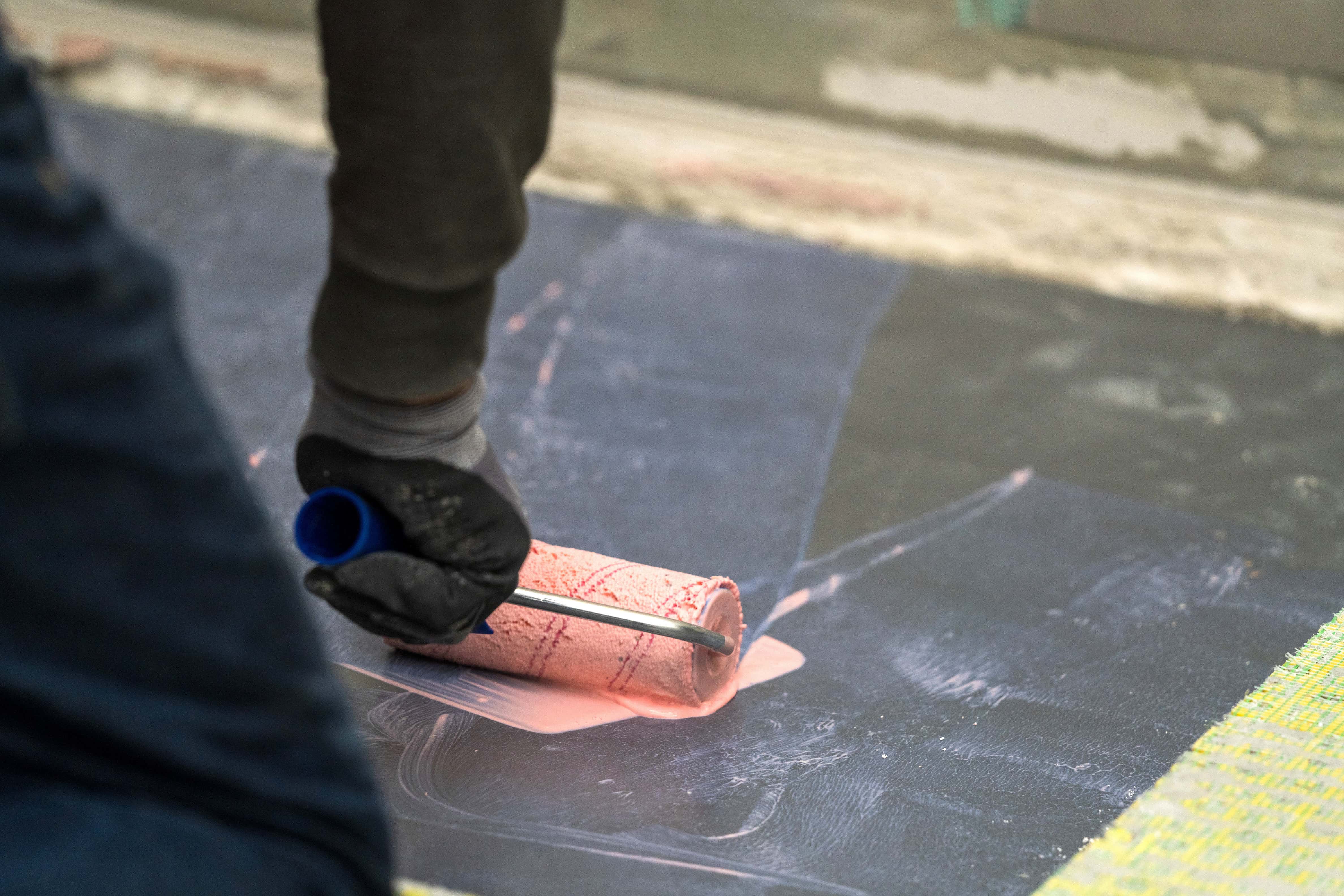 Valaki speciális alapozót hord fel egy burkolható zuhanytálcára.