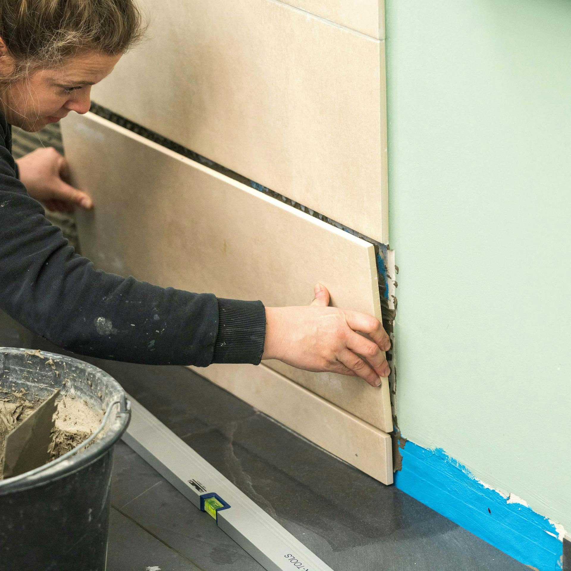 Egy hölgy csempét ragaszt fel az épített zuhanyzó falára.