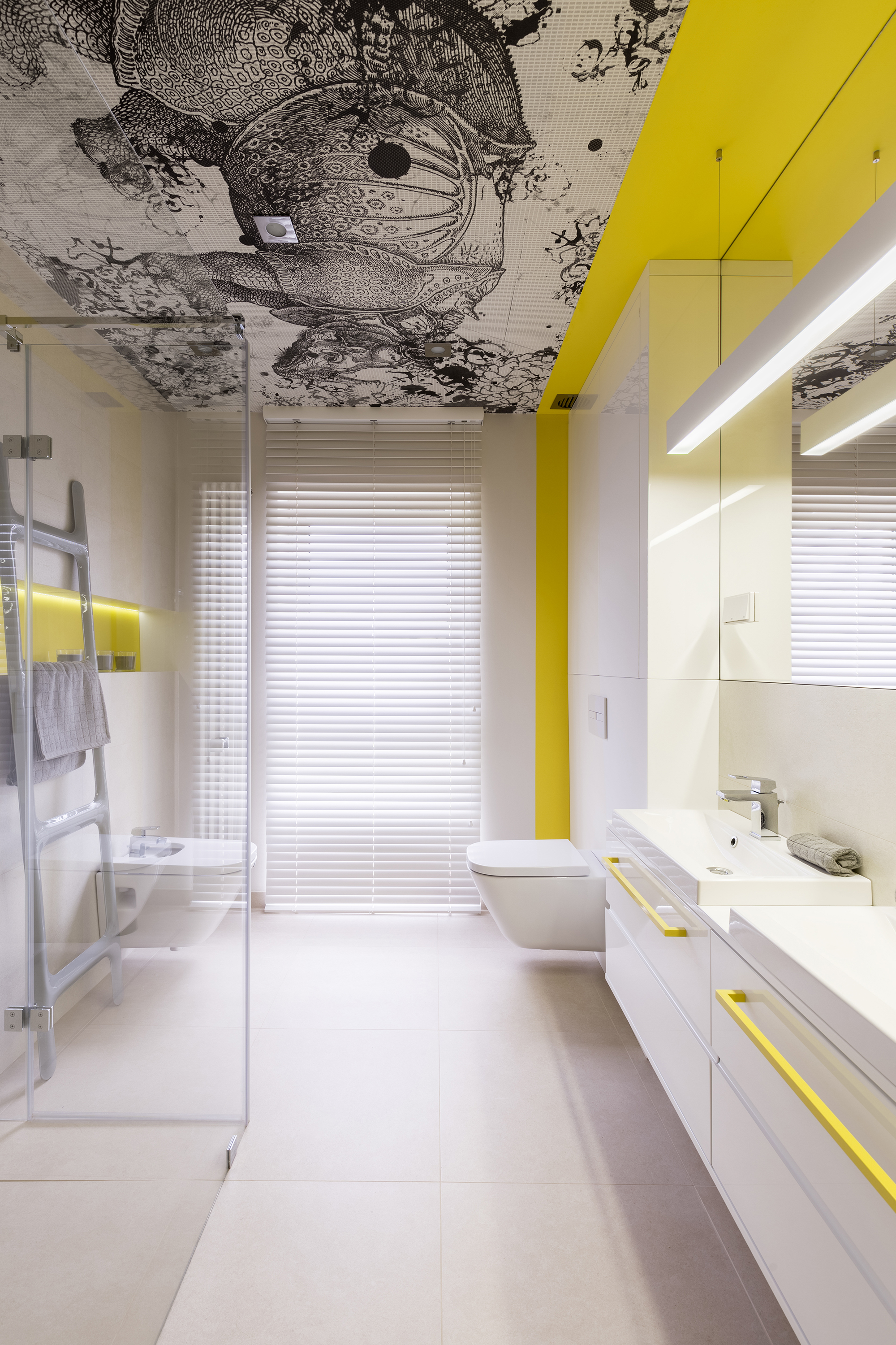 Designbad mit gelber Wand und weißen Möbeln. Die Decke ist mit schwarz-weißer Mustertapete tapeziert.