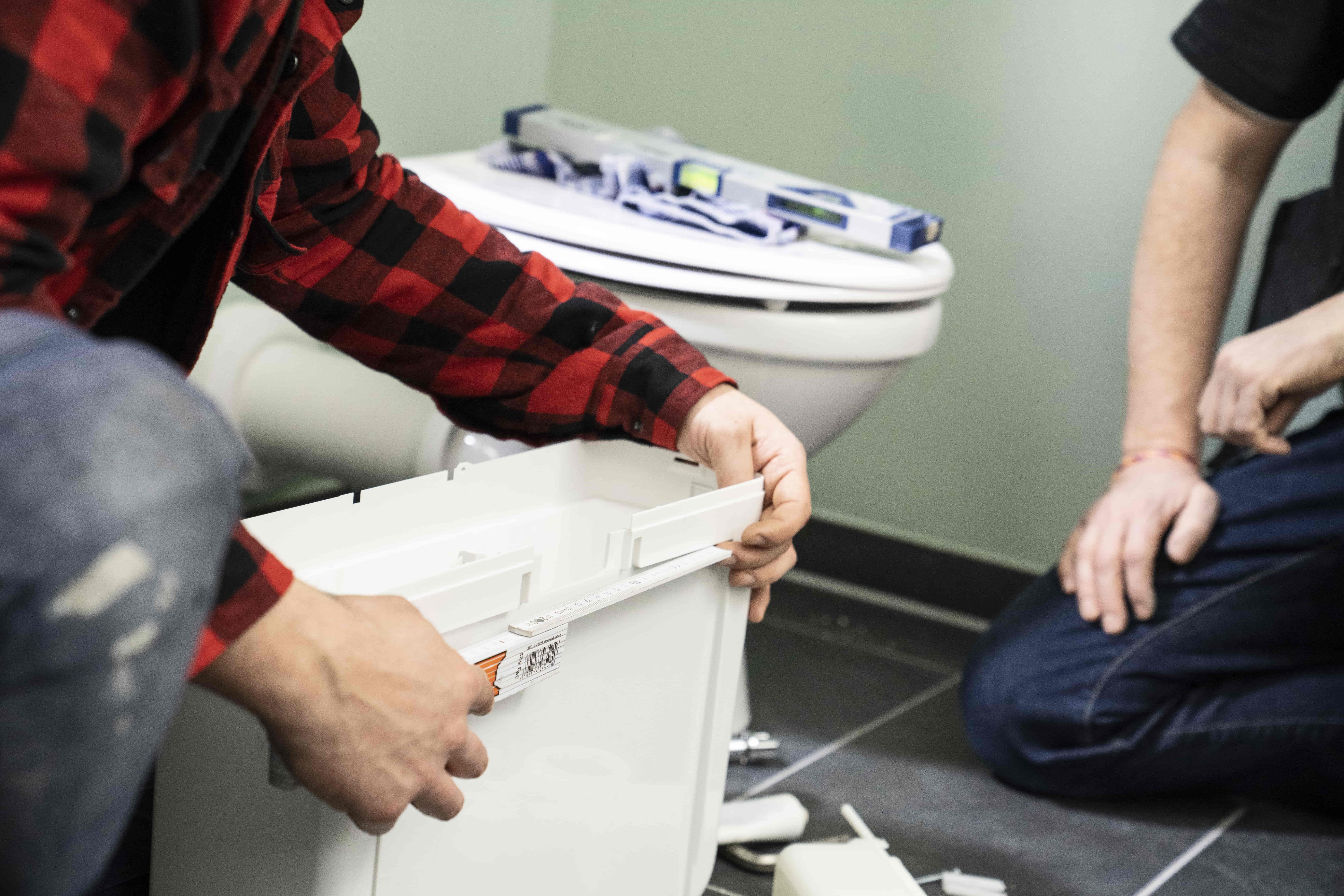 Heimwerker misst einen Spülkasten aus.