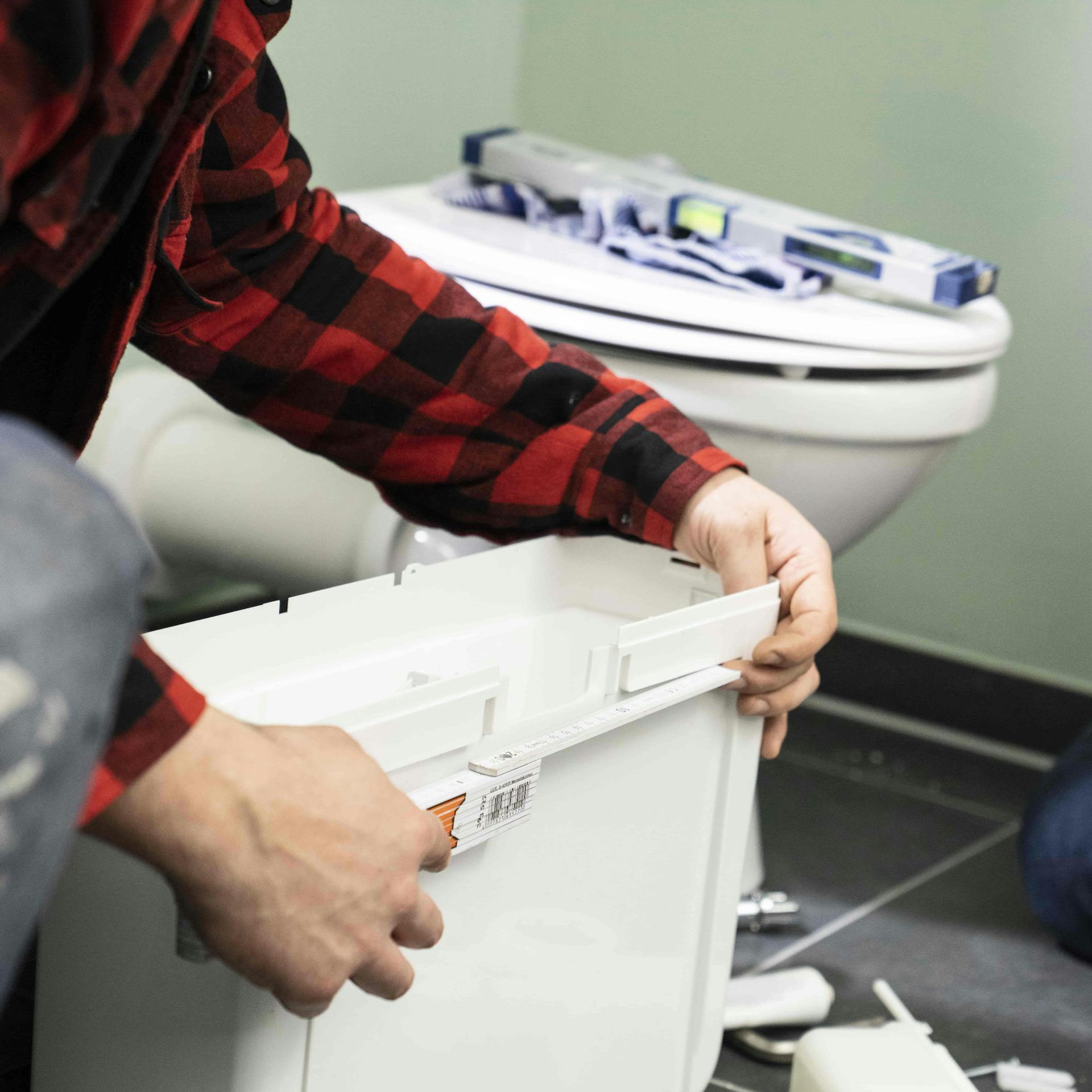 Heimwerker misst einen Spülkasten aus.