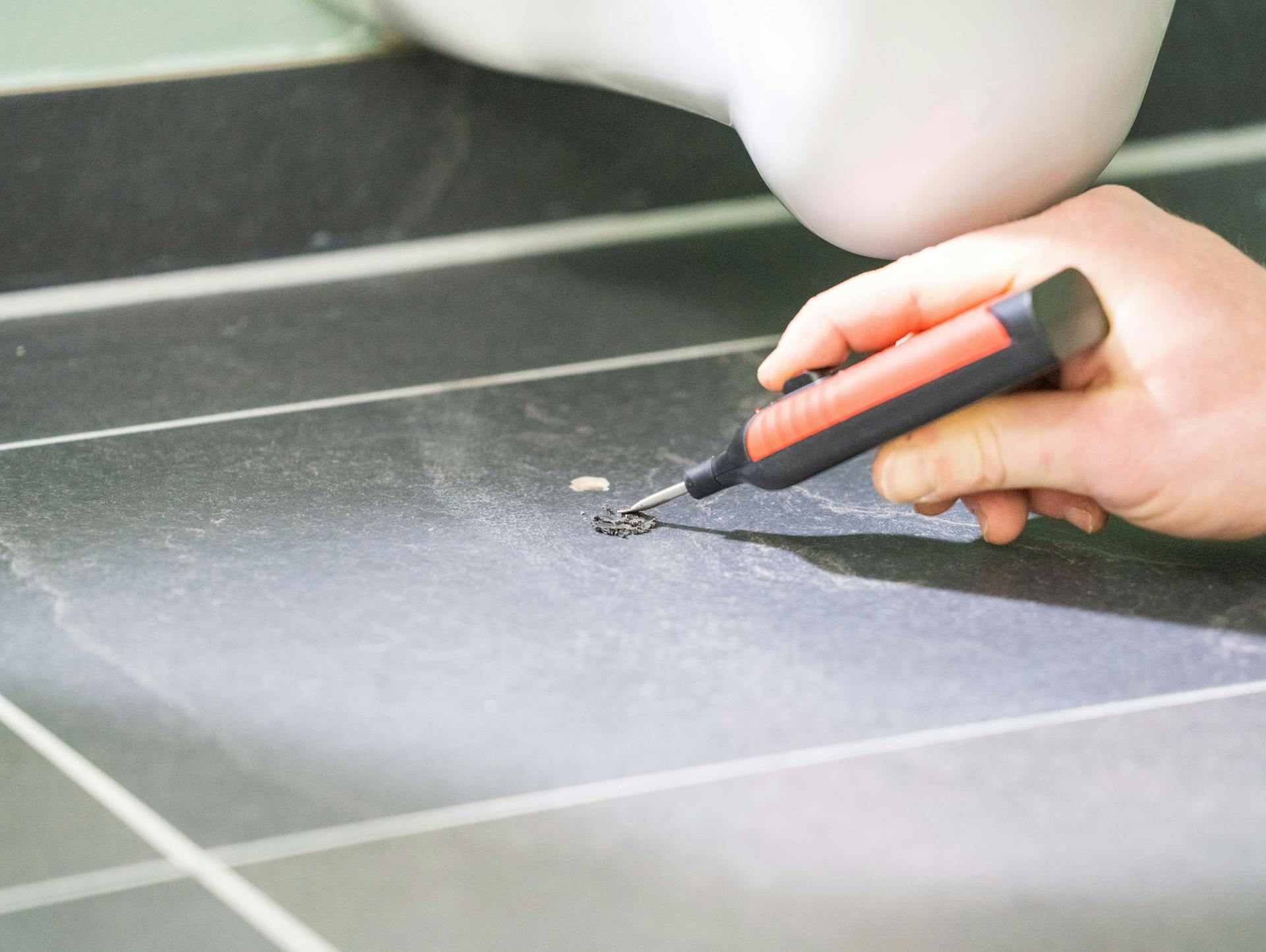 Jemand bessert ein Loch in einer dunklen Bodenfliese aus.