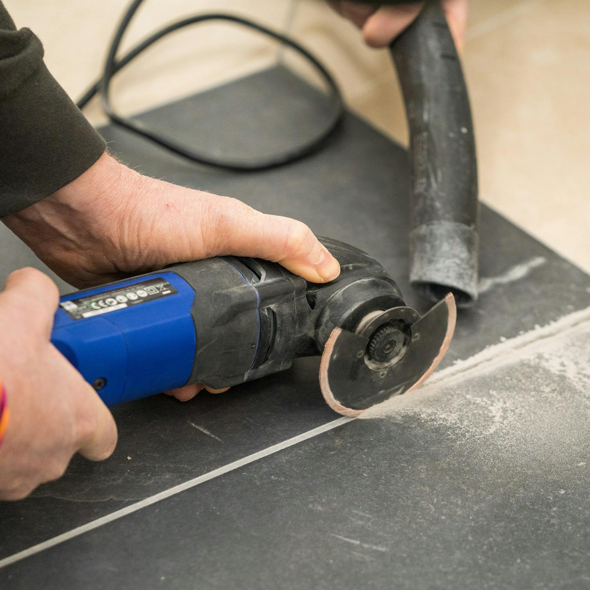 Jemand entfernt Fugenmörtel mit einem Multitool.