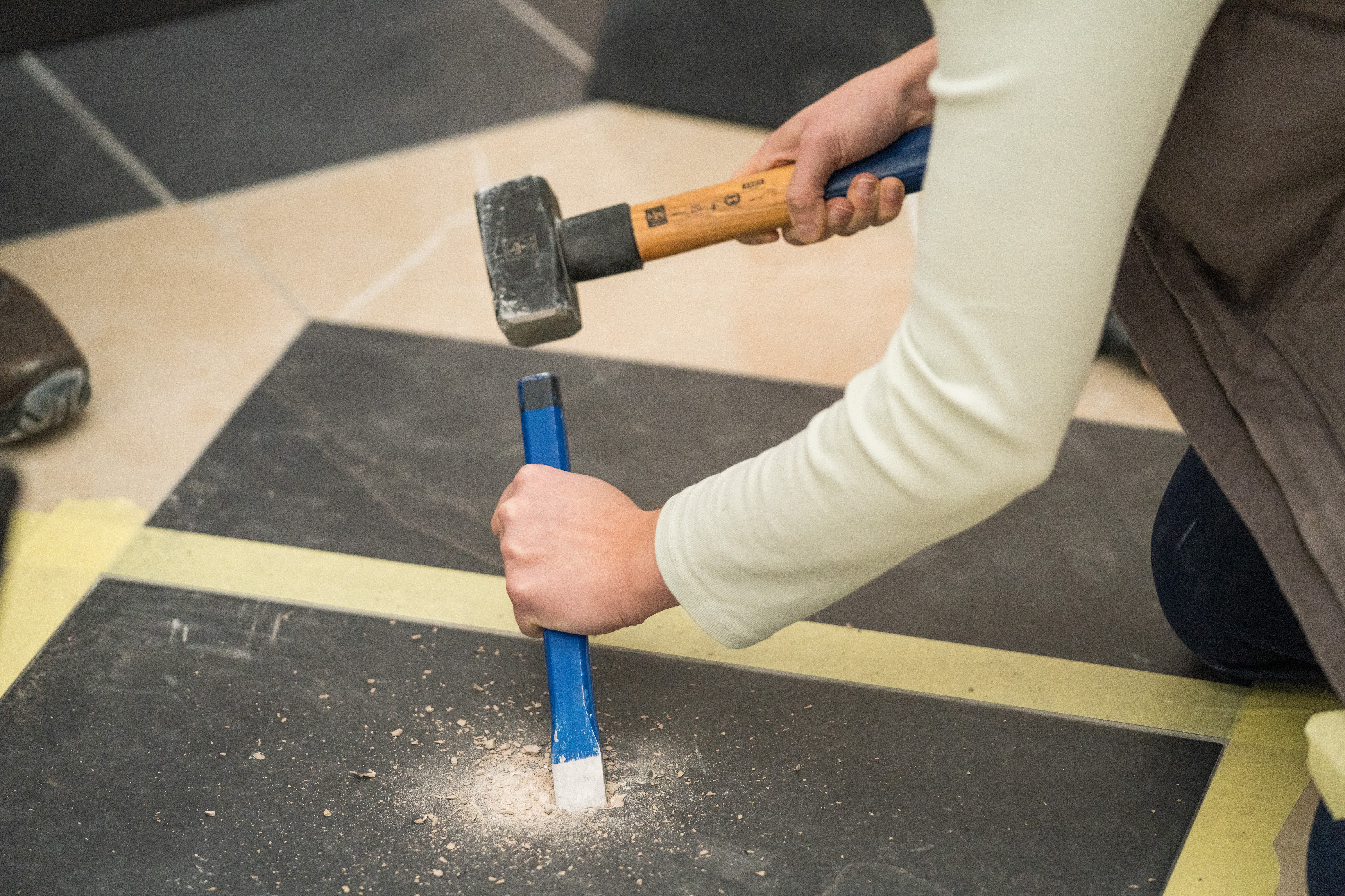 Jemand entfernt die alte Fliese mit Hammer und Meißel.