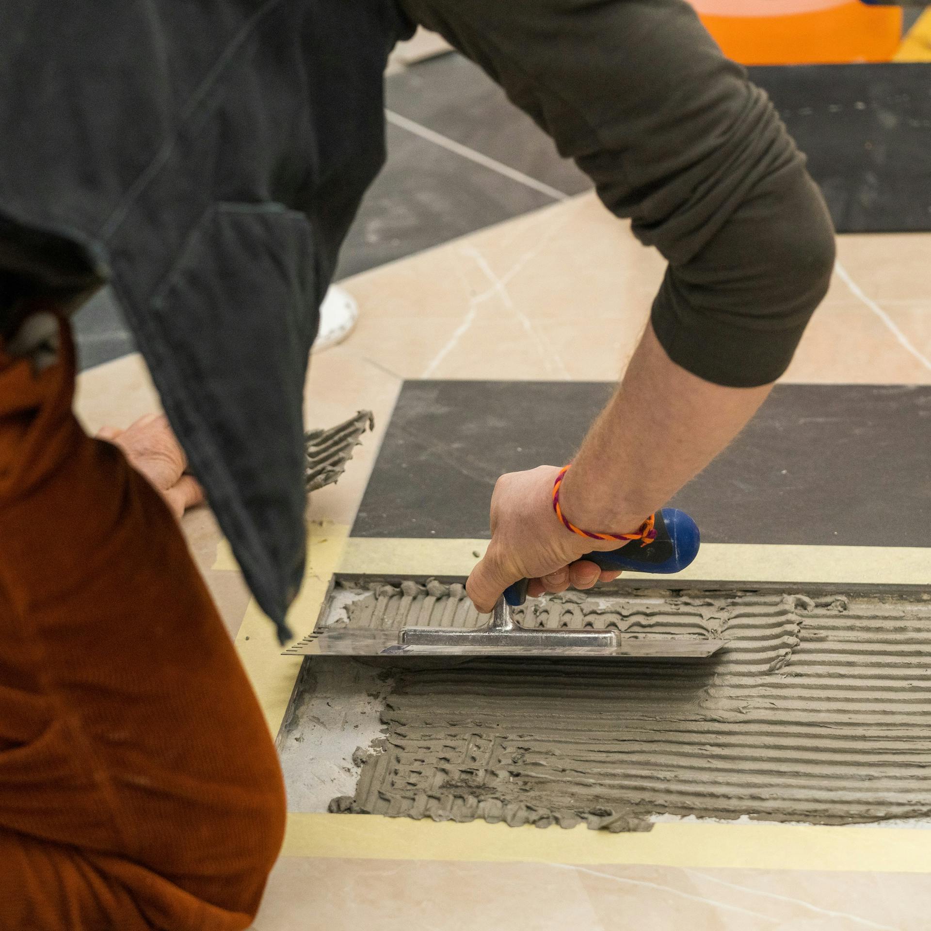 Jemand trägt Fliesenkleber auf den Boden auf.