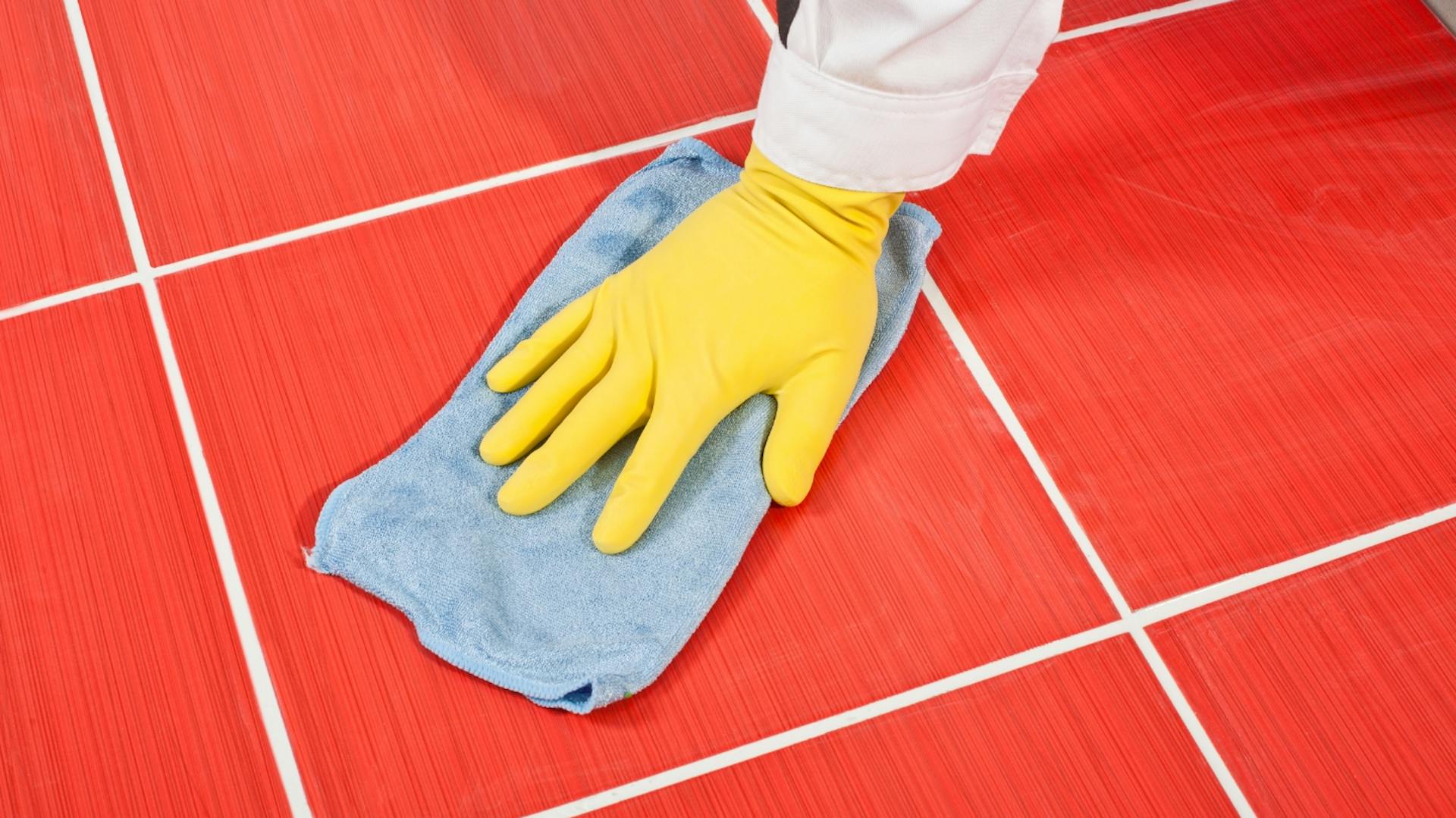 Person putzt mit blauem Mikrofasertuch rote Fliesen.