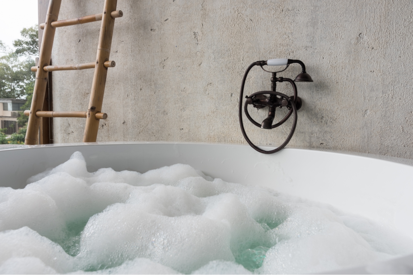 Badewanne mit Wasser und Badeschaum. Dahinter Wand aus Kalkputz.