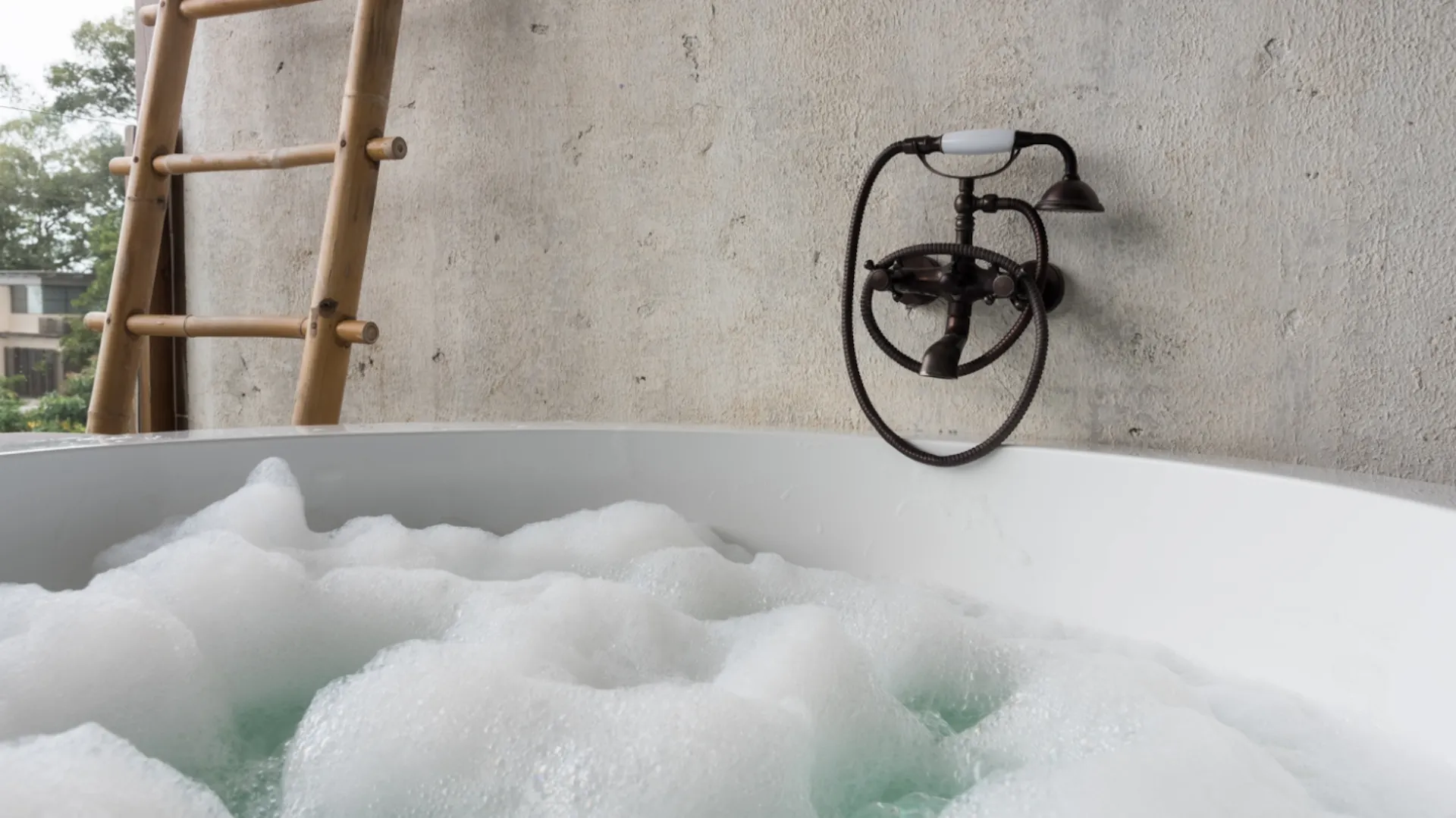 Badewanne mit Wasser und Badeschaum. Dahinter Wand aus Kalkputz.