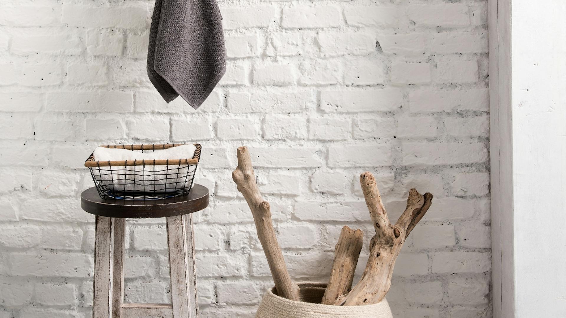 Ast als Handtuchhalterung, darunter ein Hocker und ein Korb mit weiteren Ästen.