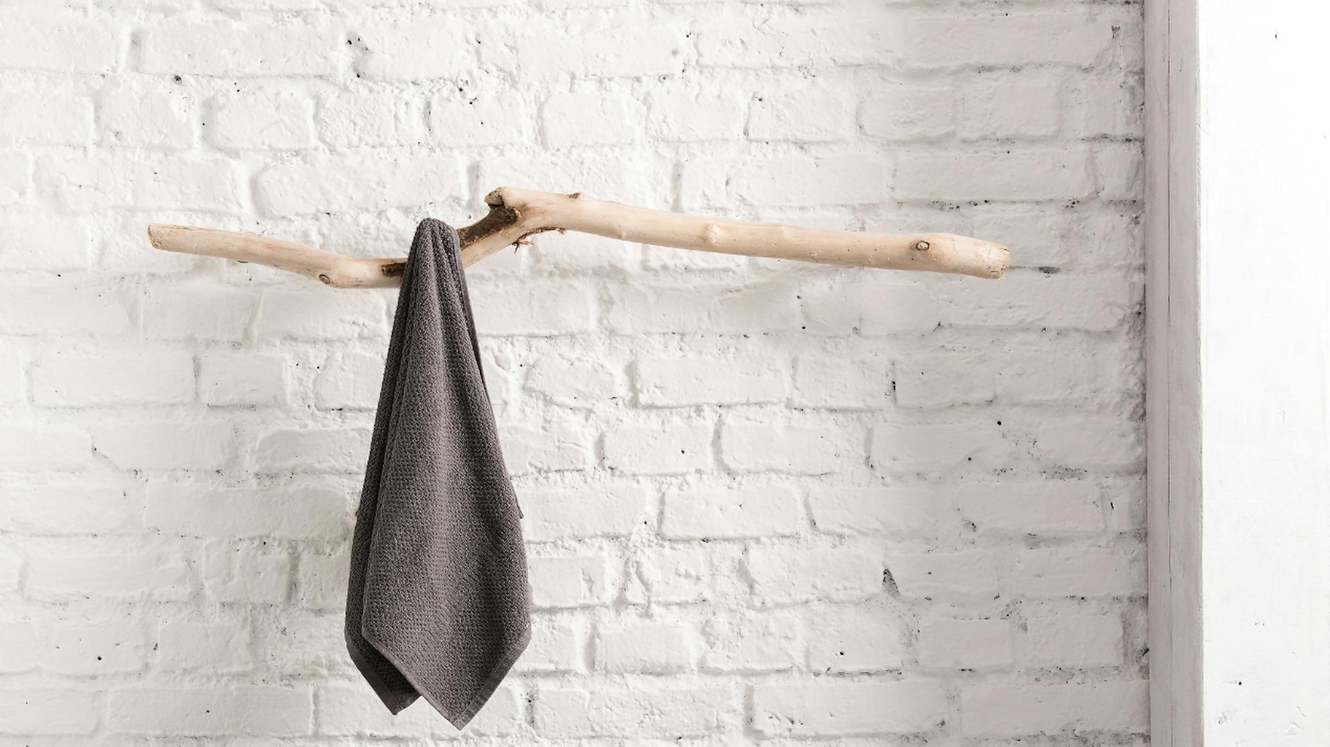 Handtuch hängt auf einem frei schwingenden Ast. Darunter steht ein Hocke und ein Korb mit Holzstücken.