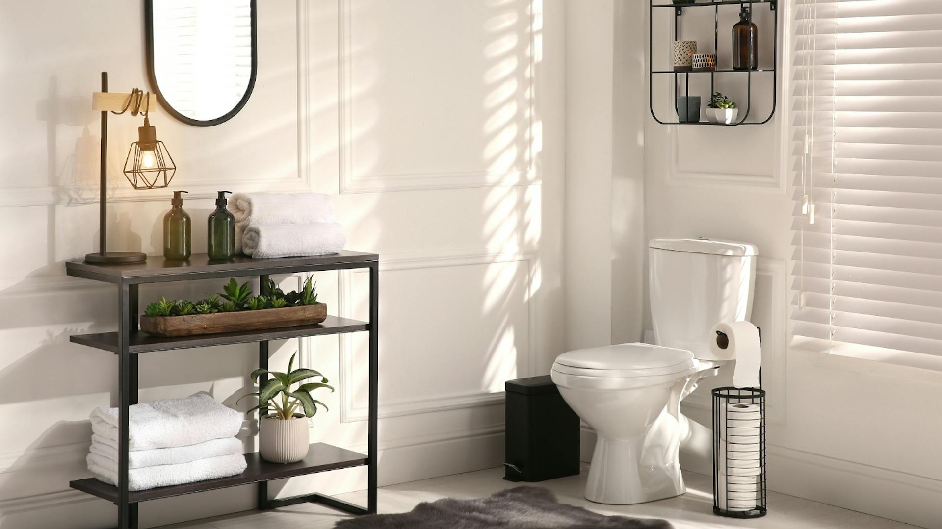 Regal aus dunklem Metall mit weißen Handtüchern, Lampe im industriellen Design und Pflanze. Seitlich weiße Toilette, darüber Wandregal aus schwarzem Metall.