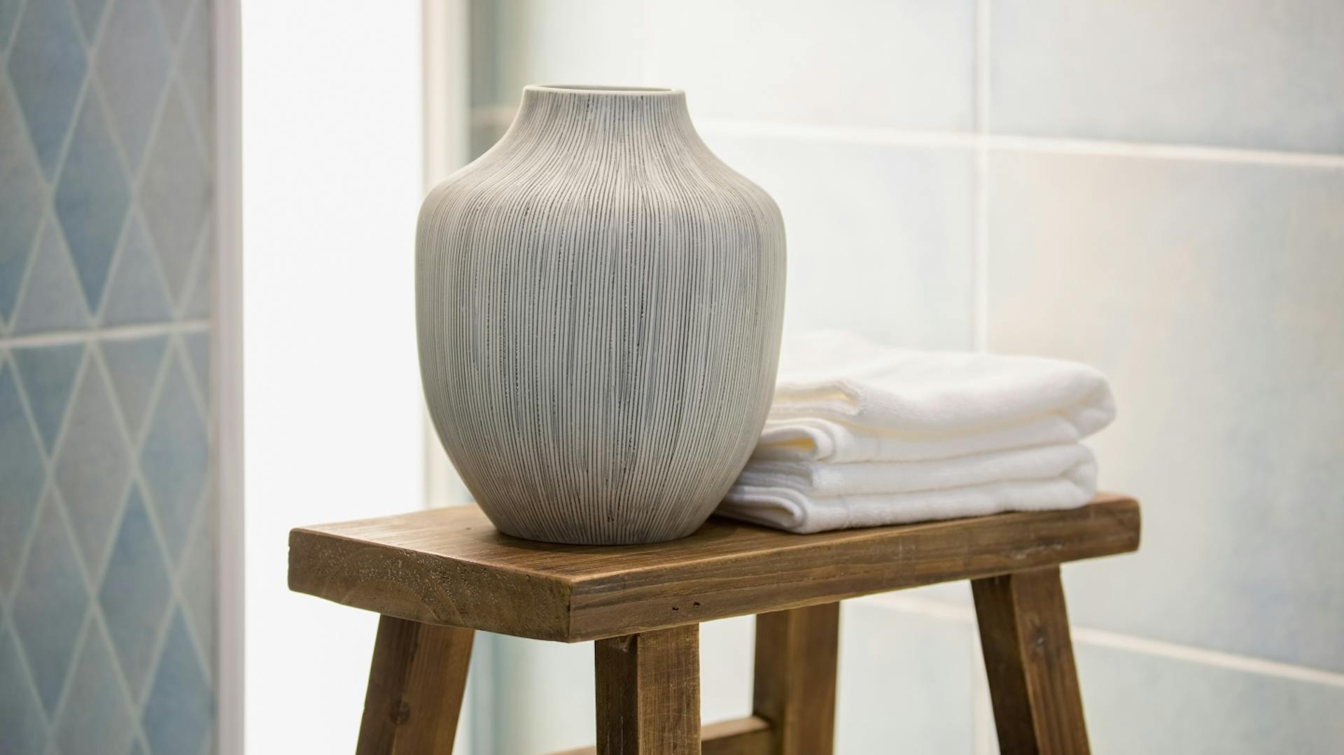 Auf einem Holzhocker steht eine weiße Vase, daneben liegen kleine weiße Handtücher.