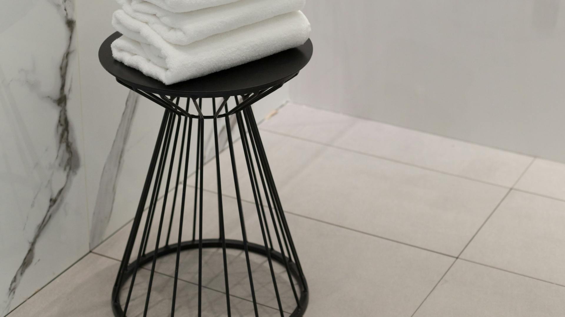 Schwarzer Metallhocker, auf dem weiße gefaltete Handtücher liegen.