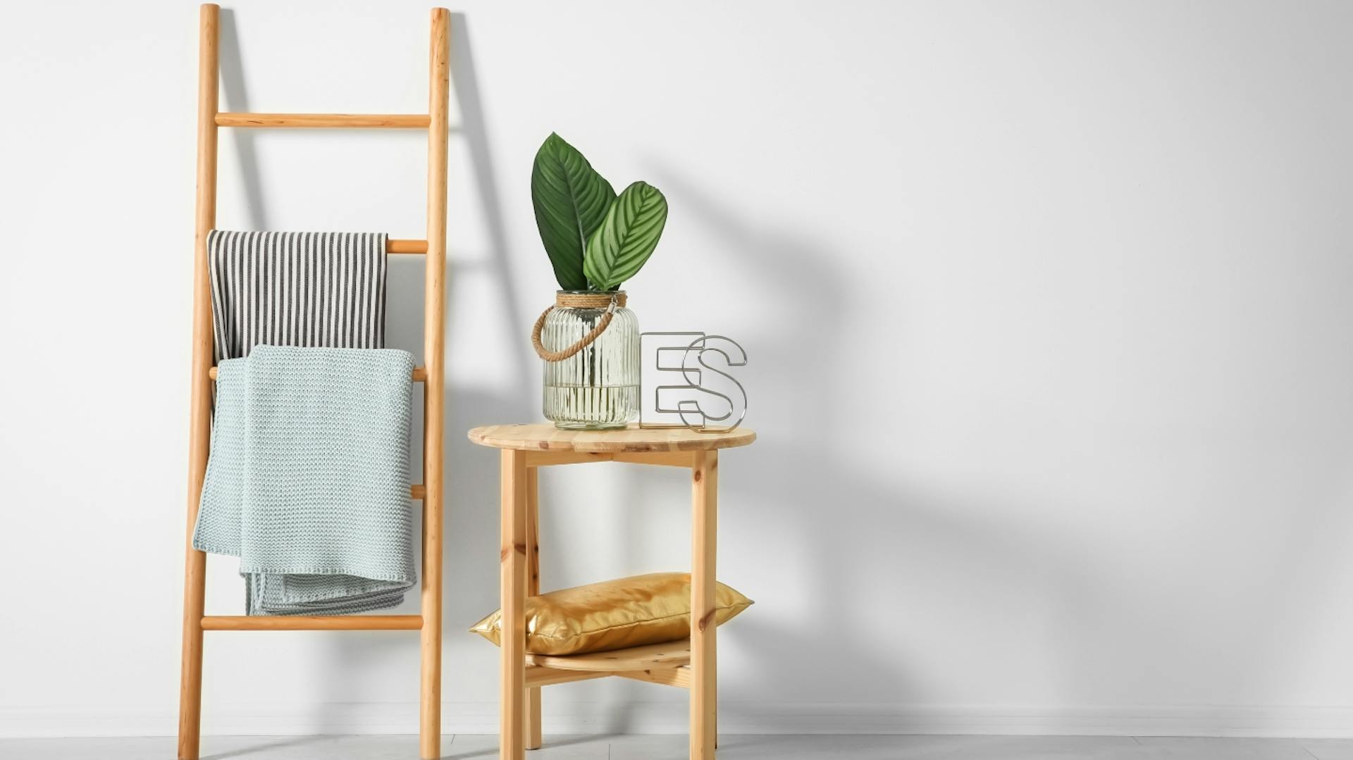Holzleiter mit grauem und hellblauen Handtuch. Daneben ein Hocker mit einer grünen Pflanze.