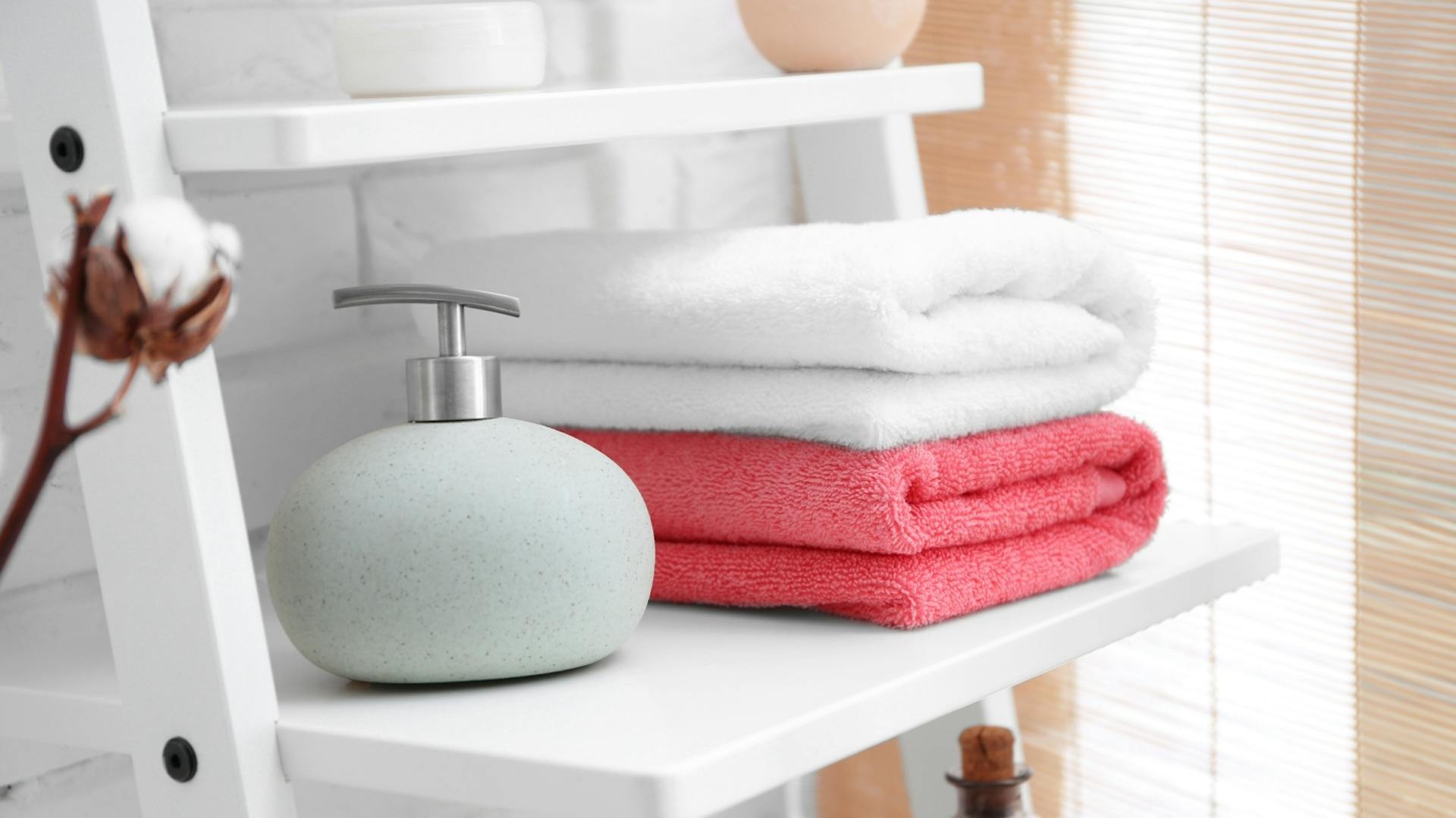 Weißes Leiterregal mit Seifenspender und zwei Handtüchern in rot und weiß.