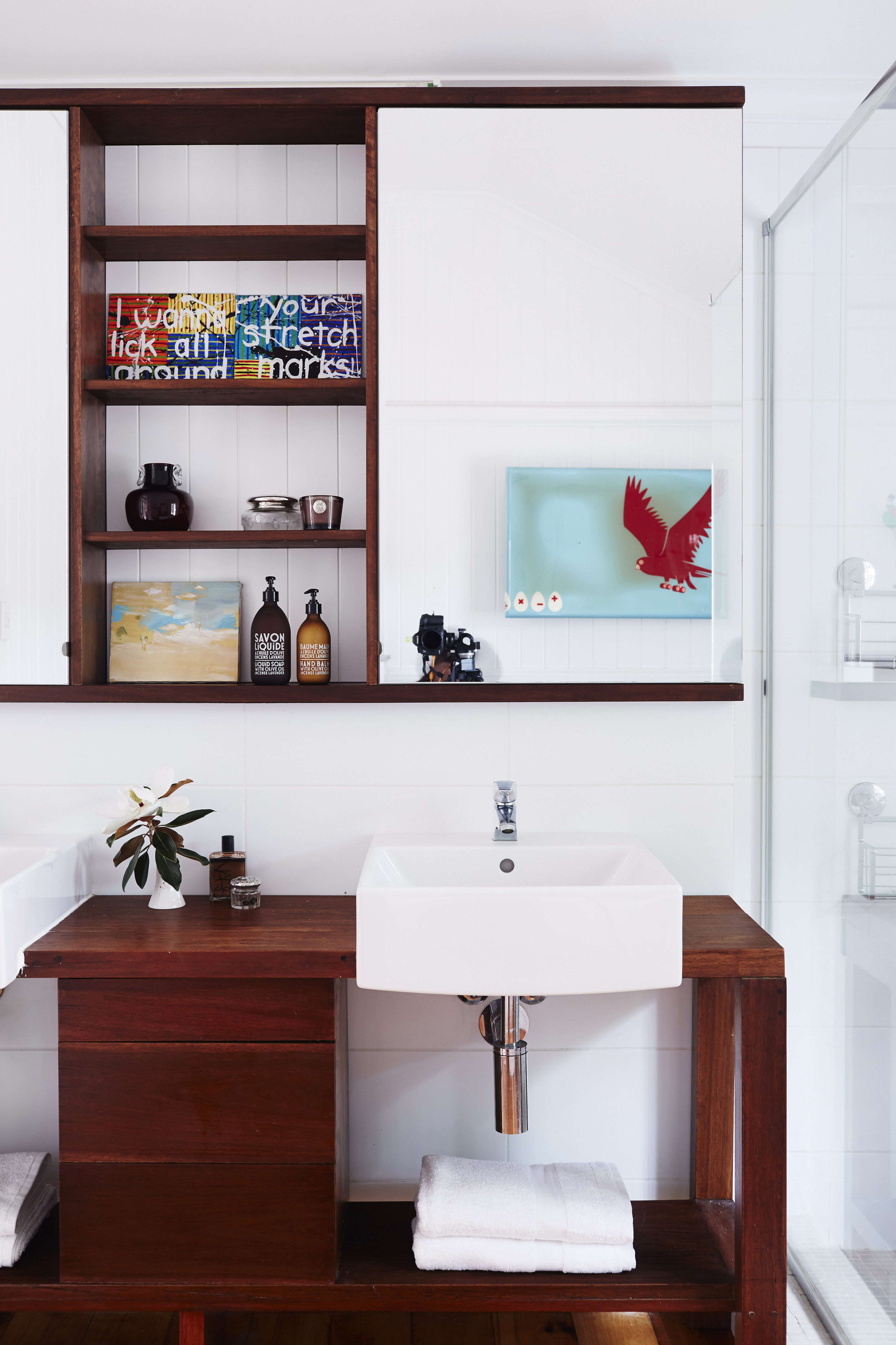 Ein Badezimmer mit Waschtisch und Schrank aus einer dunklen Holzsorte mit einem weißen Waschbecken und Fliesen.