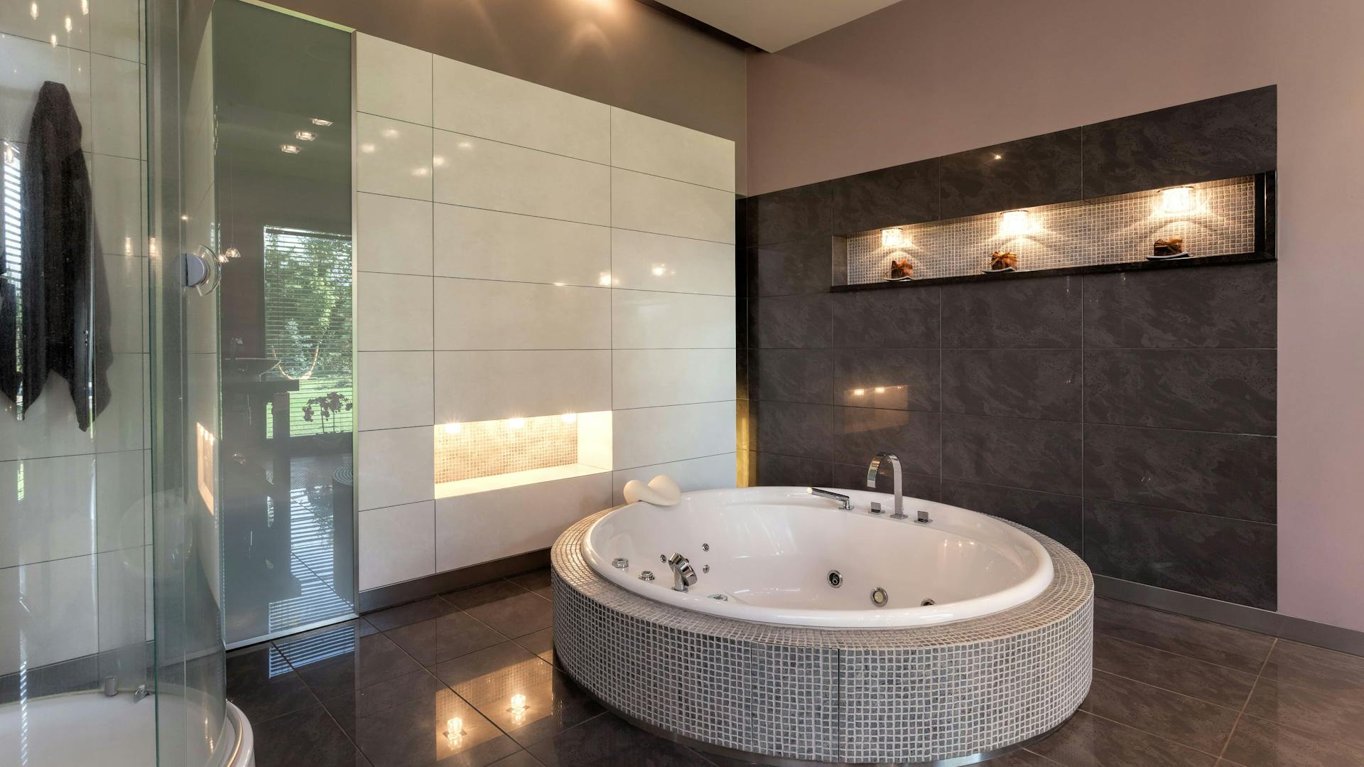 Bagno con vasca rotonda indipendente e illuminazione indiretta a parete e a soffitto.