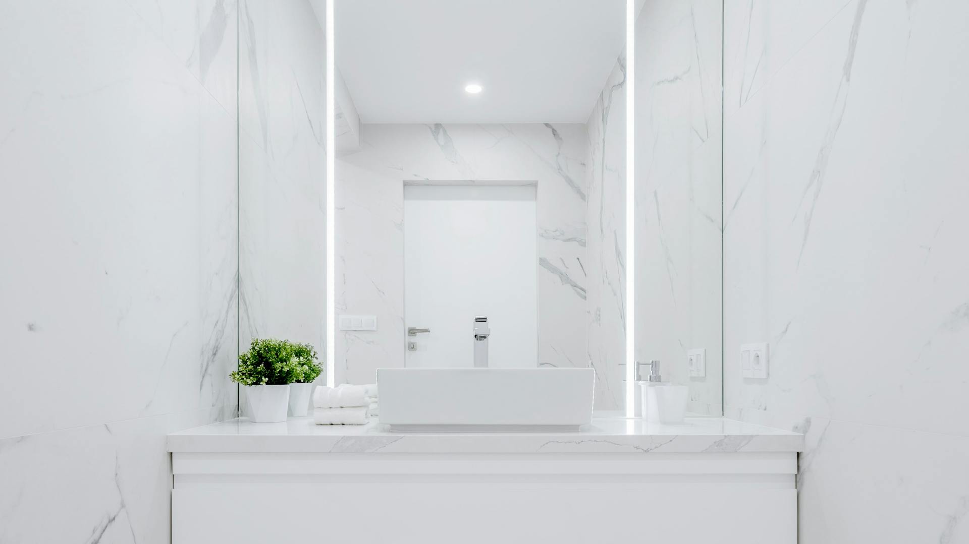 Specchio con barre luminose integrate in un bagno bianco.