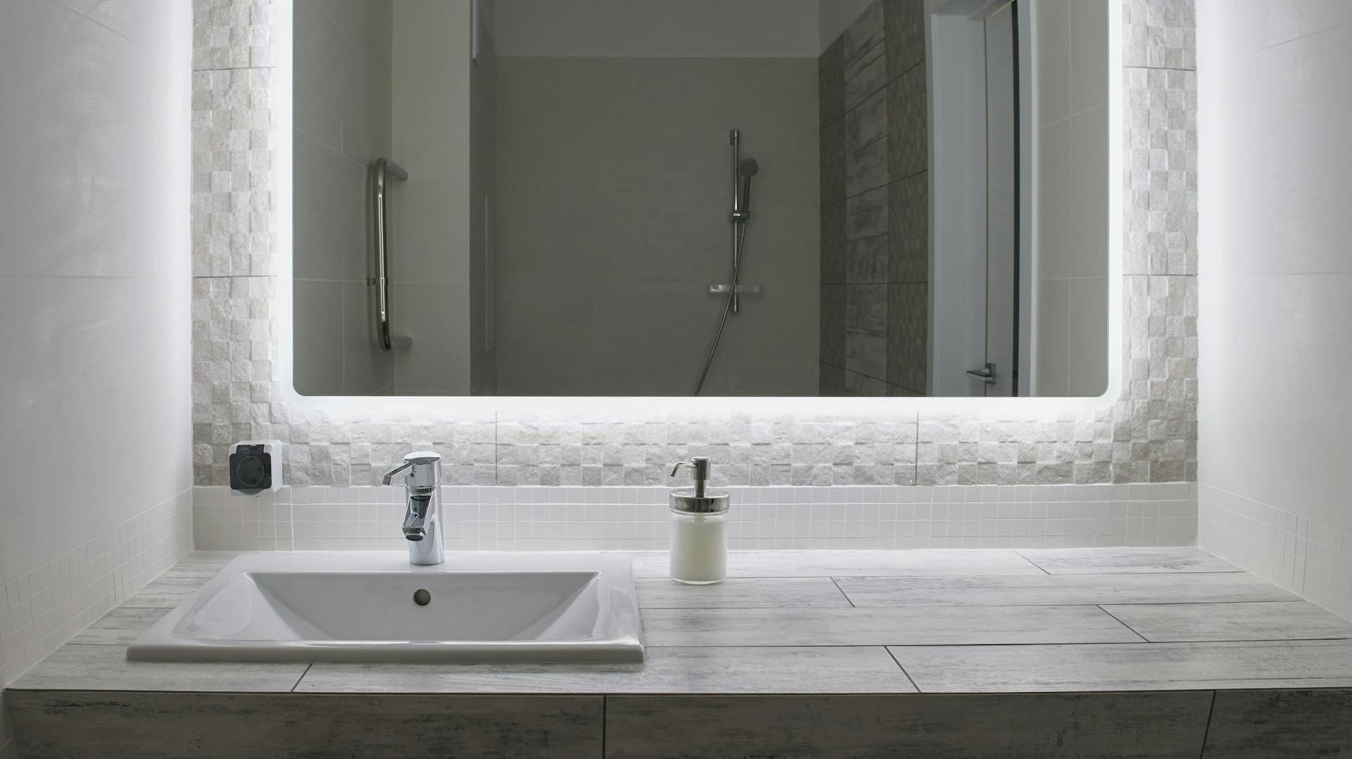 Grande specchio con illuminazione indiretta sopra un lavabo chiaro.