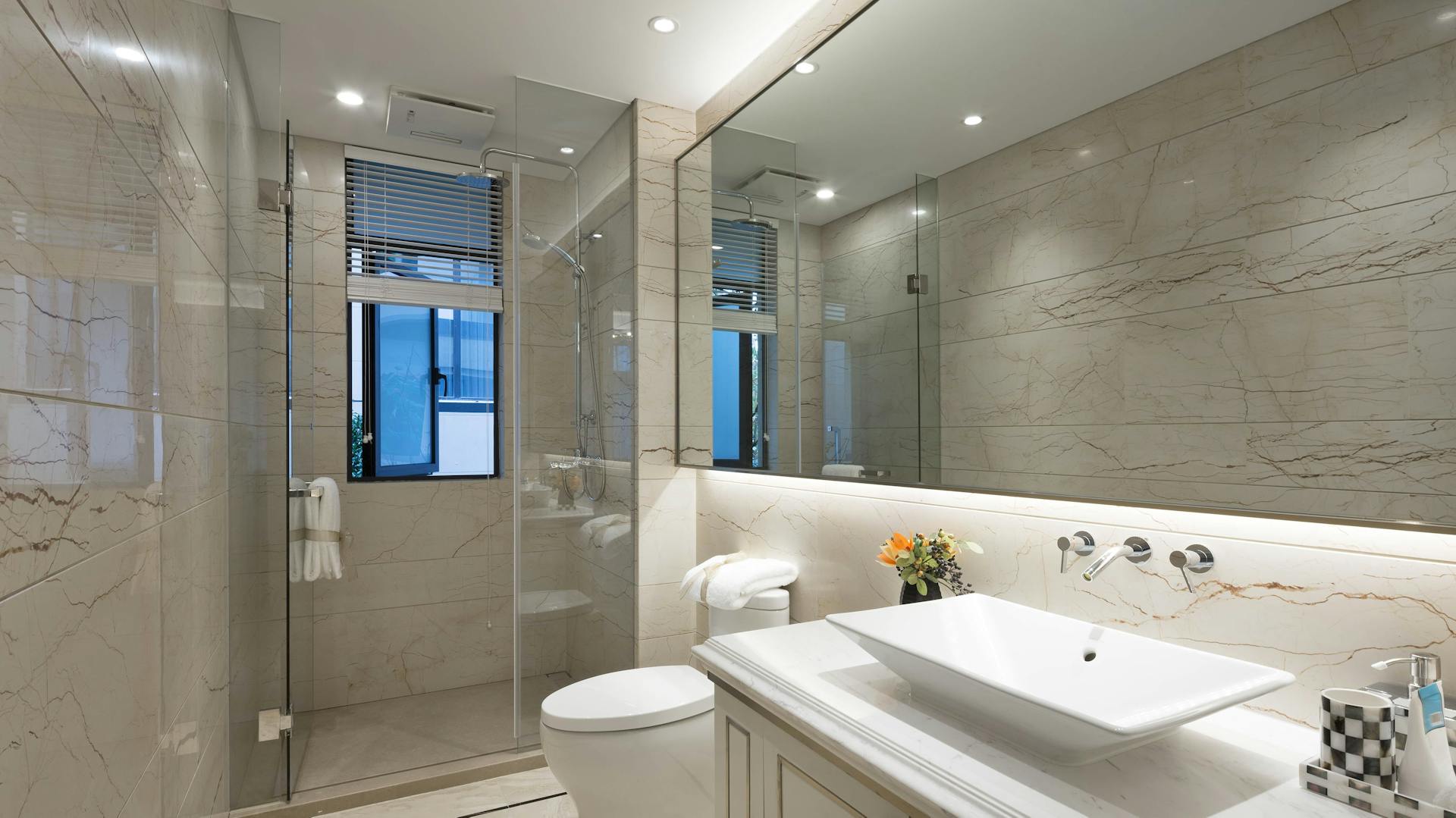 Badezimmer mit Waschtisch, Toilette, Dusche und großem Spiegel mit indirekter Beleuchtung.