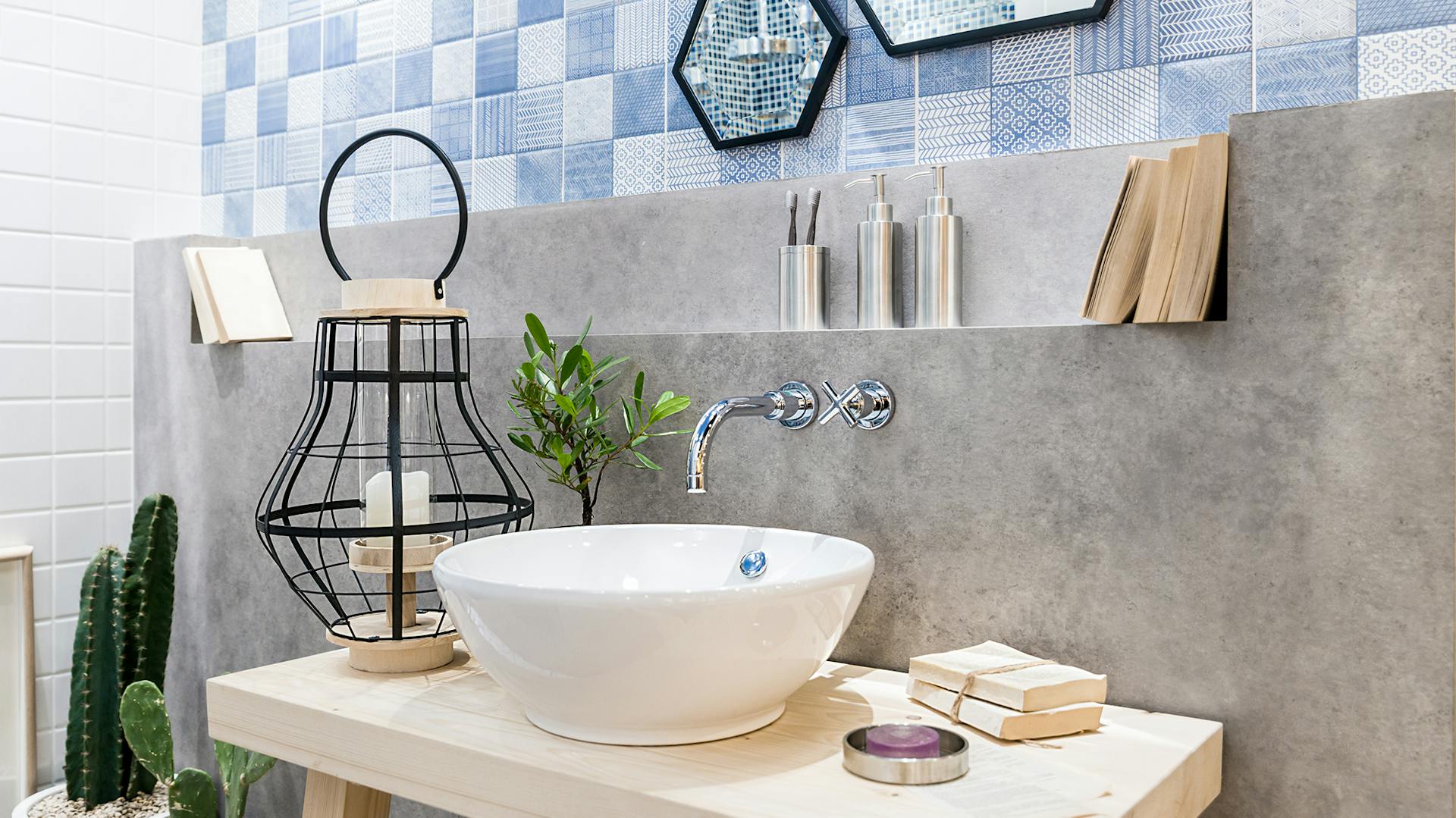 Lavabo bianco su ripiano in legno. Muro di cemento sullo sfondo, piastrelle azzurre a mosaico.