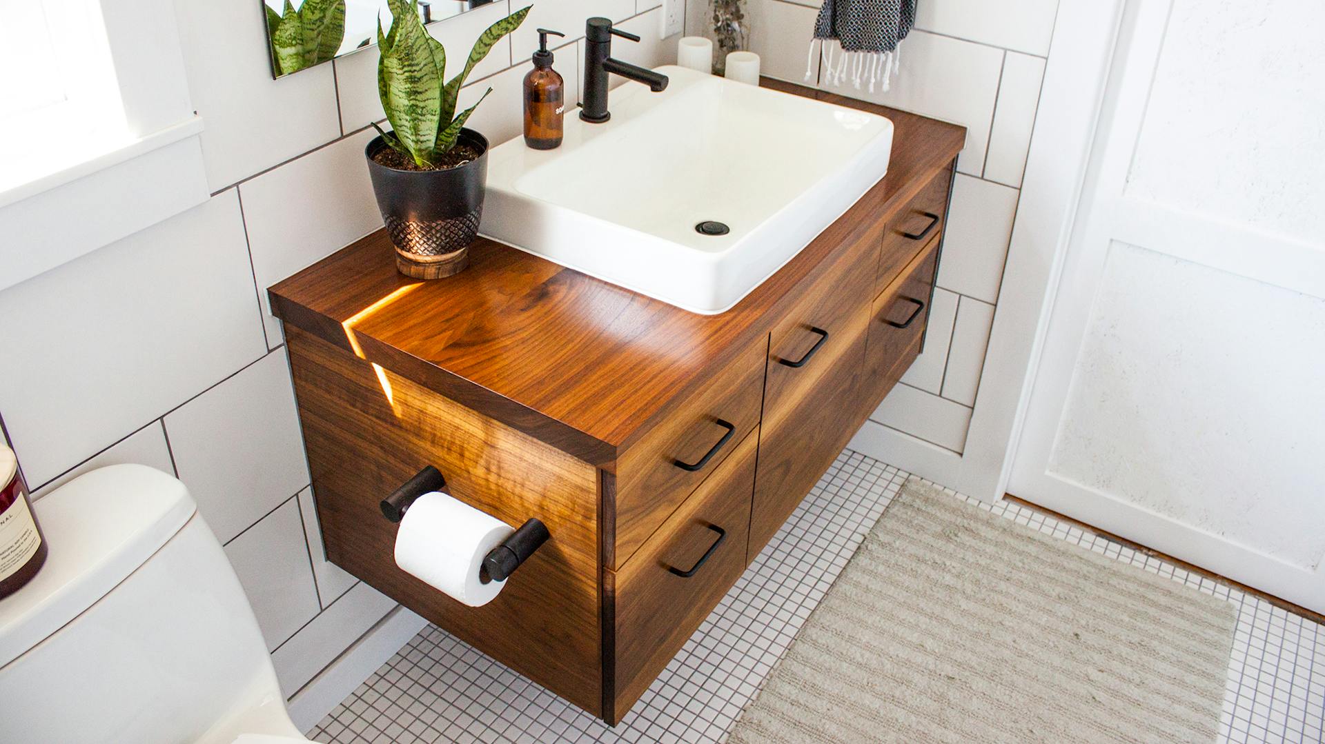 Mobile lavabo in legno scuro con lavabo bianco e porta carta igienica laterale.