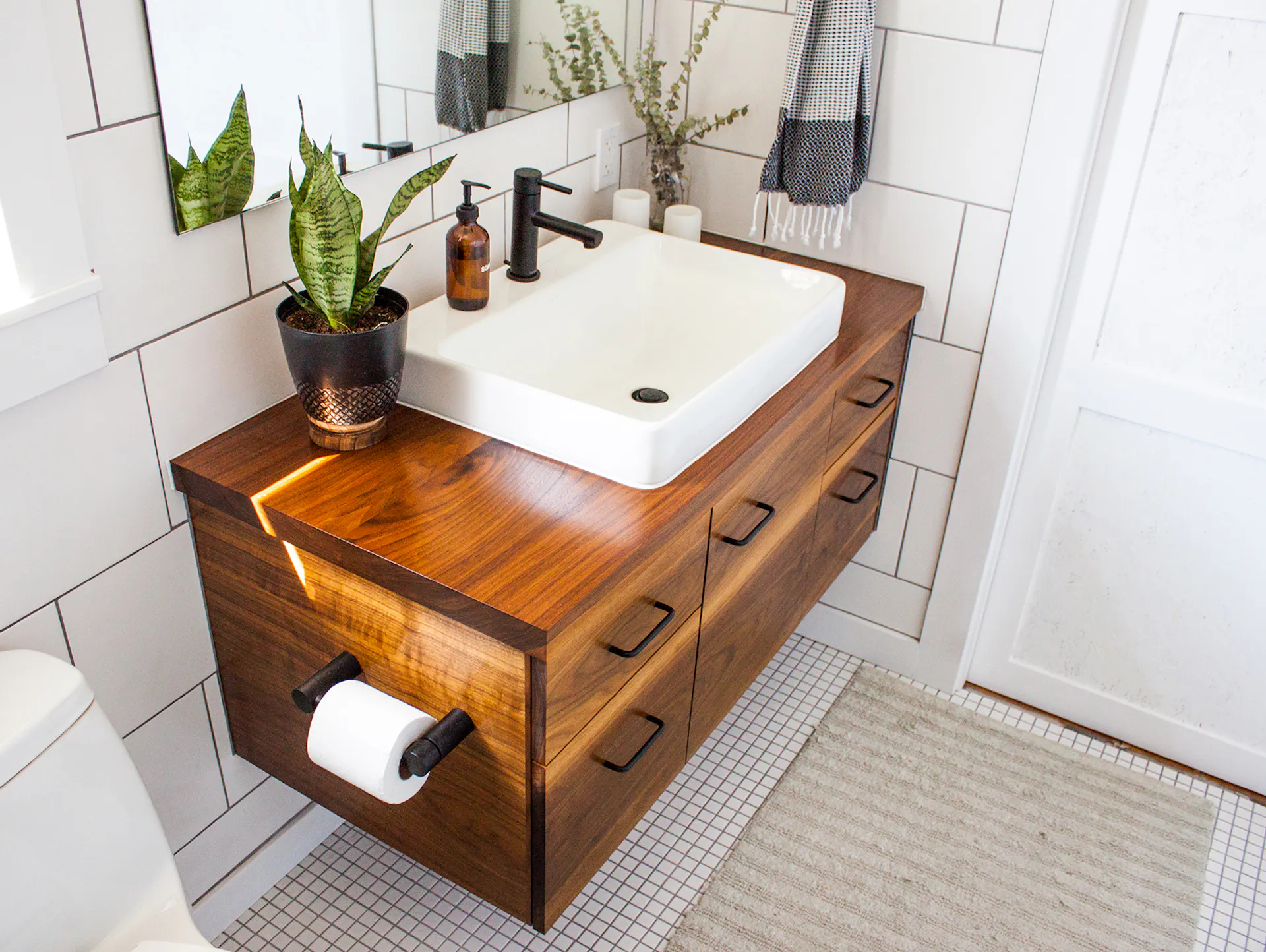 Mobile lavabo in legno scuro con lavabo bianco e porta carta igienica laterale.