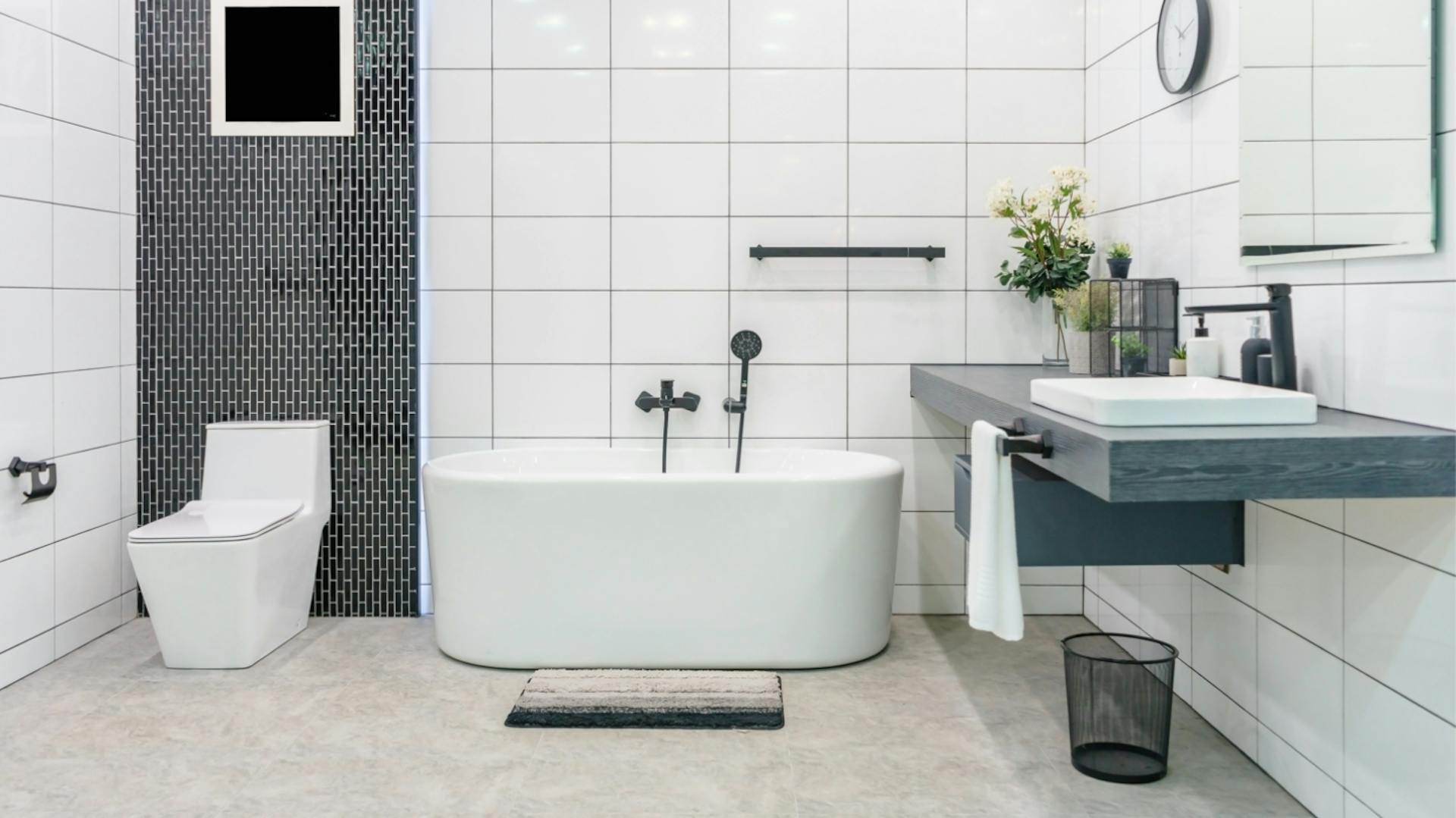 Weißes Badezimmer mit Badewanne. Hinter der Toilette ist ein schwarz-gefliester Wandstreifen.