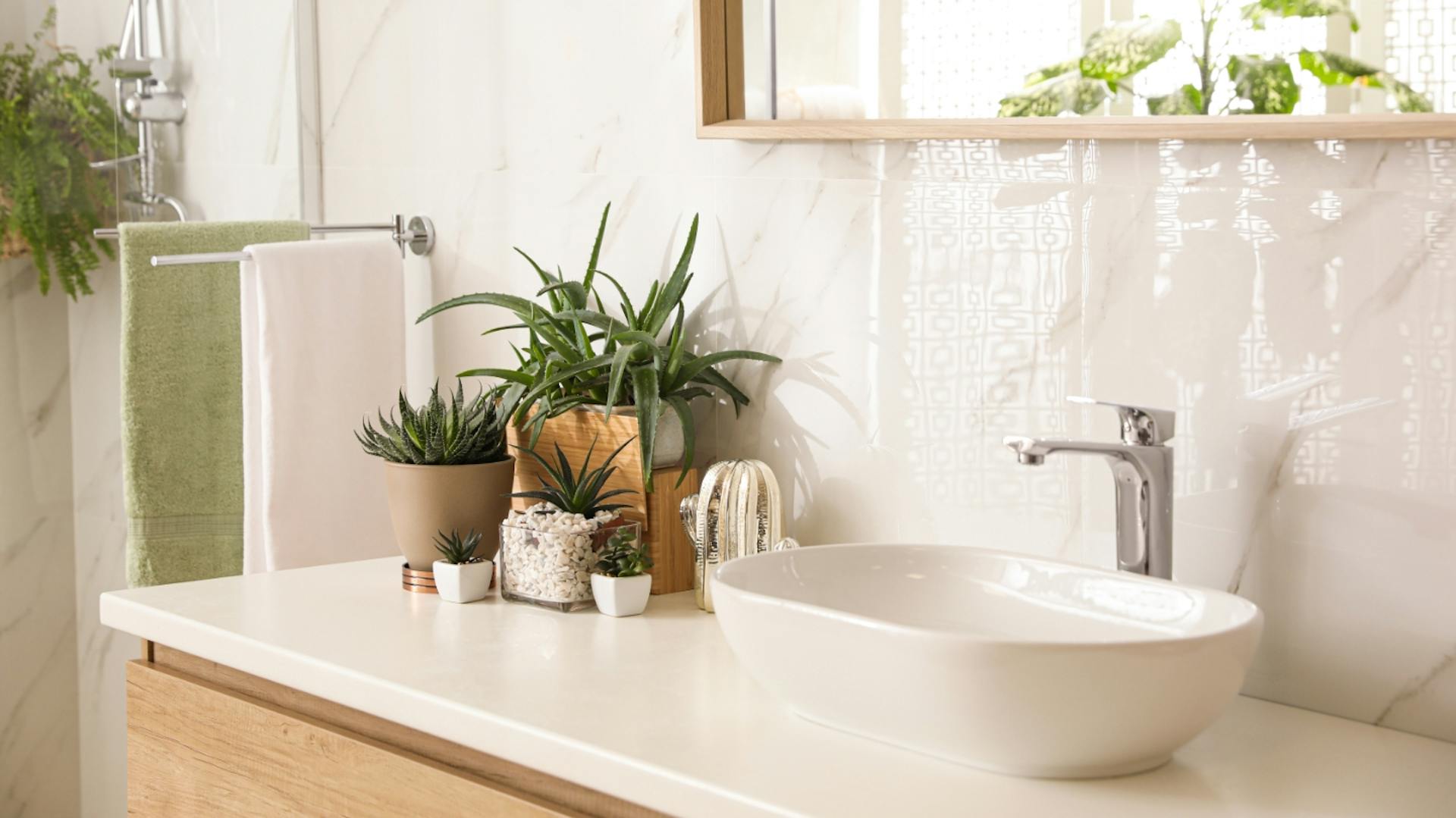 Piastrelle bianche davanti a un mobile lavabo in legno con lavabo bianco e piante.